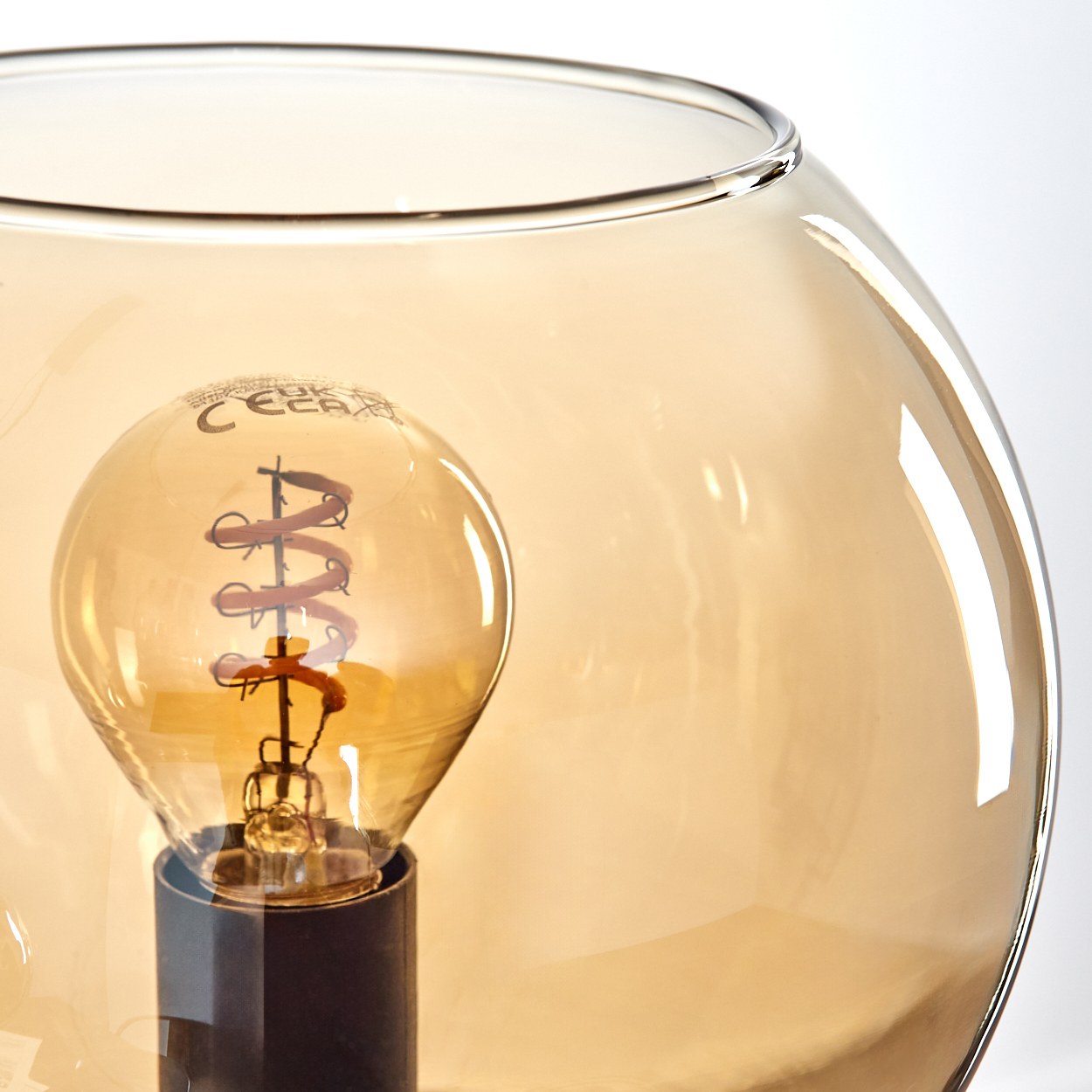 Nahaufnahme einer Glühbirne in einer Glaskugel. Die Glühbirne hat einen spiralförmigen Glühfaden, und das Glas hat einen goldenen Farbton.