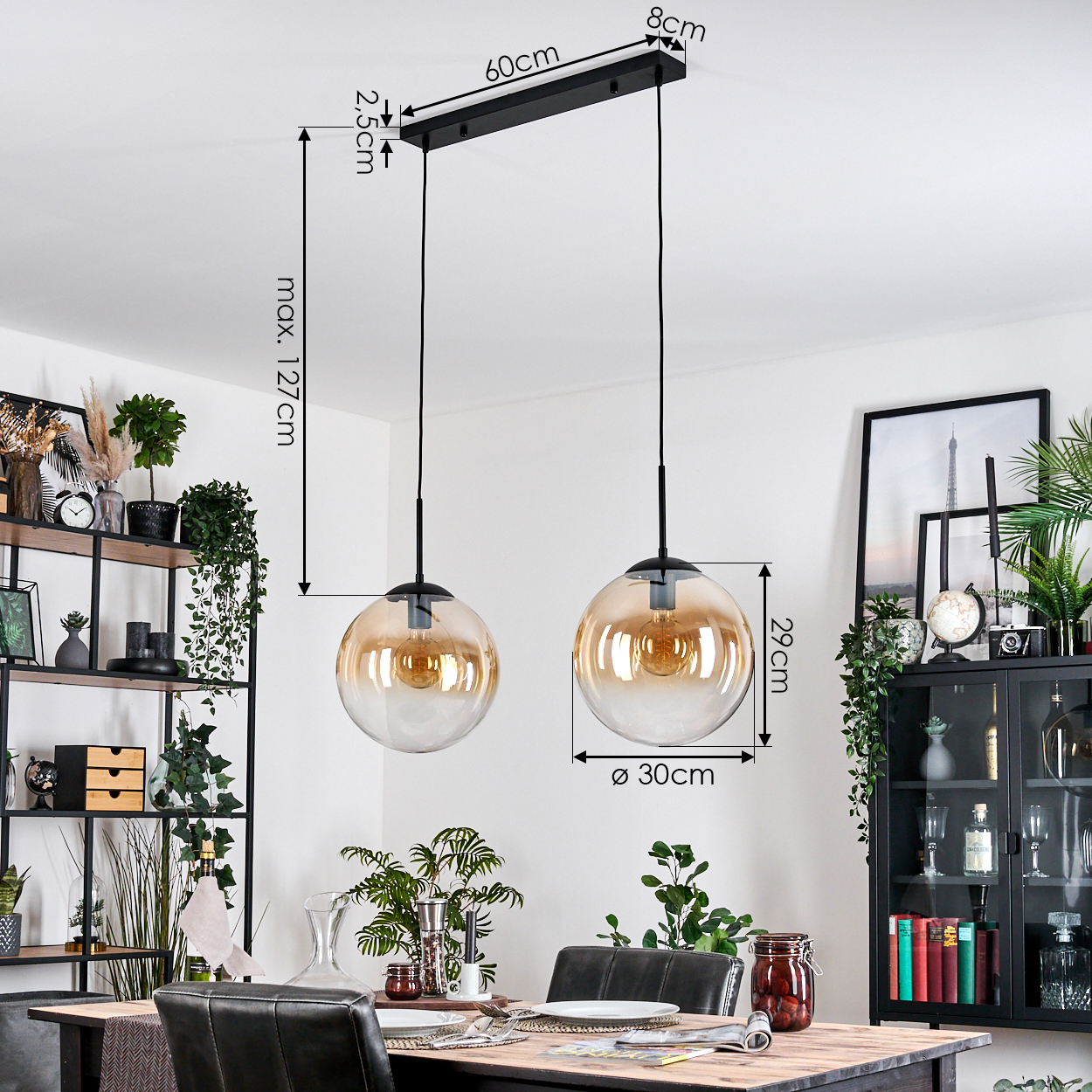 Zwei bernsteinfarbene Glaskugel-Pendelleuchten hängen über einem Holzesstisch. Regale und ein Schrank mit Pflanzen und Dekor sind sichtbar.