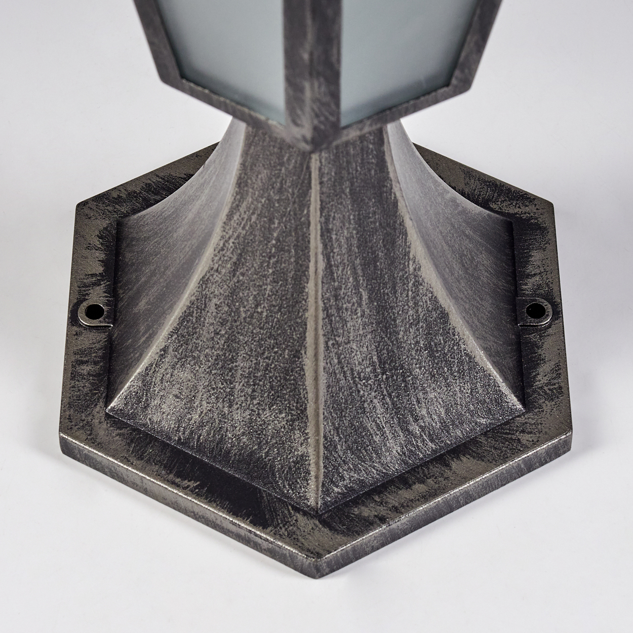 Nahaufnahme einer metallischen Außenlampe. Die Lampe hat einen sechseckigen Sockel, einen konischen Körper und eine glaseingeschlossene Oberseite. Weißer Hintergrund.