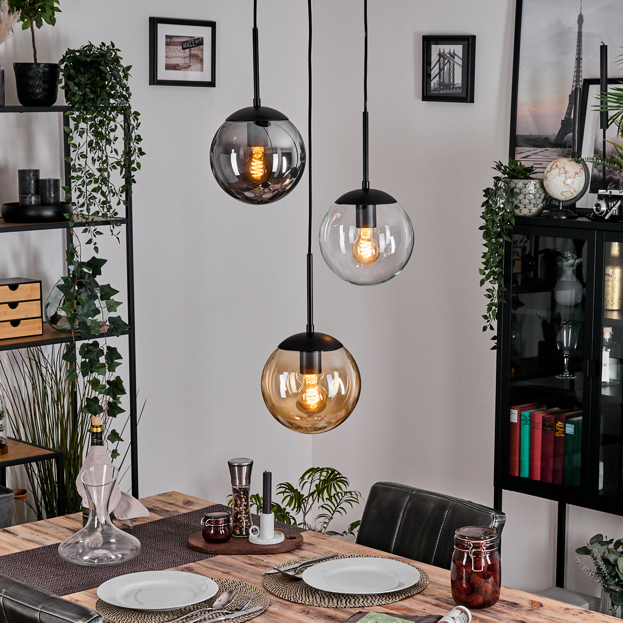 Esszimmer-Szene mit drei hängenden Kugelleuchten, einem Holztisch für das Abendessen und einem schwarzen Bücherregal.