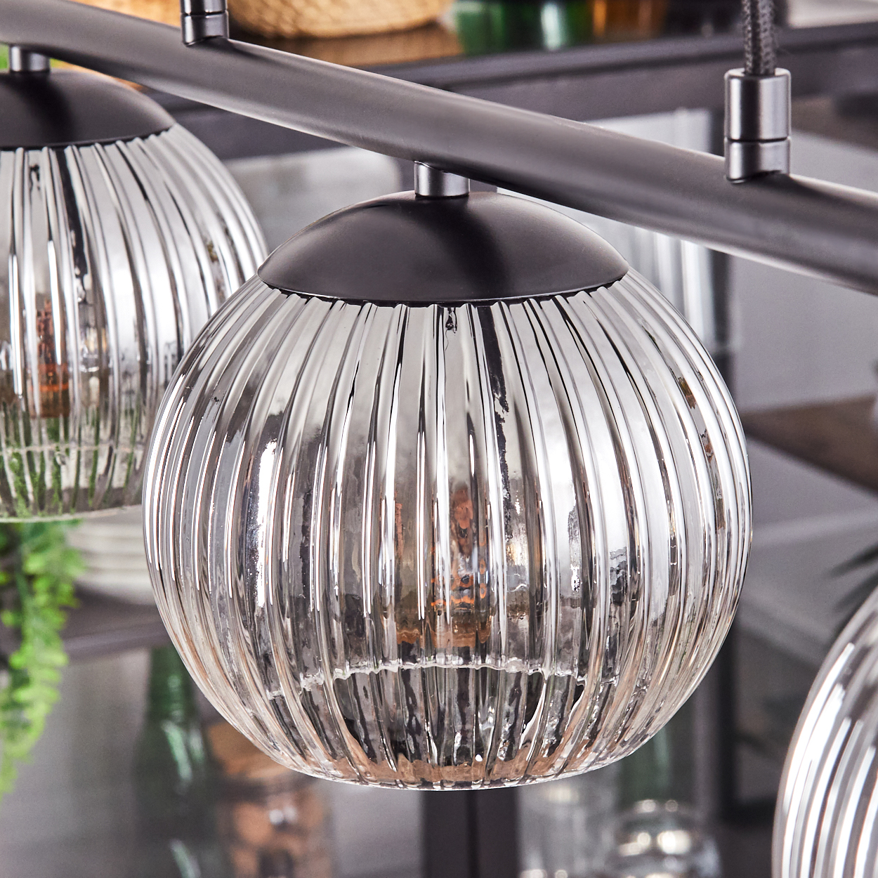 Nahaufnahme einer modernen Leuchte mit drei Glaskugelschirmen. Die Schirme sind gerippt, klar und reflektieren Licht. Eine dunkle Metallstange hält sie.