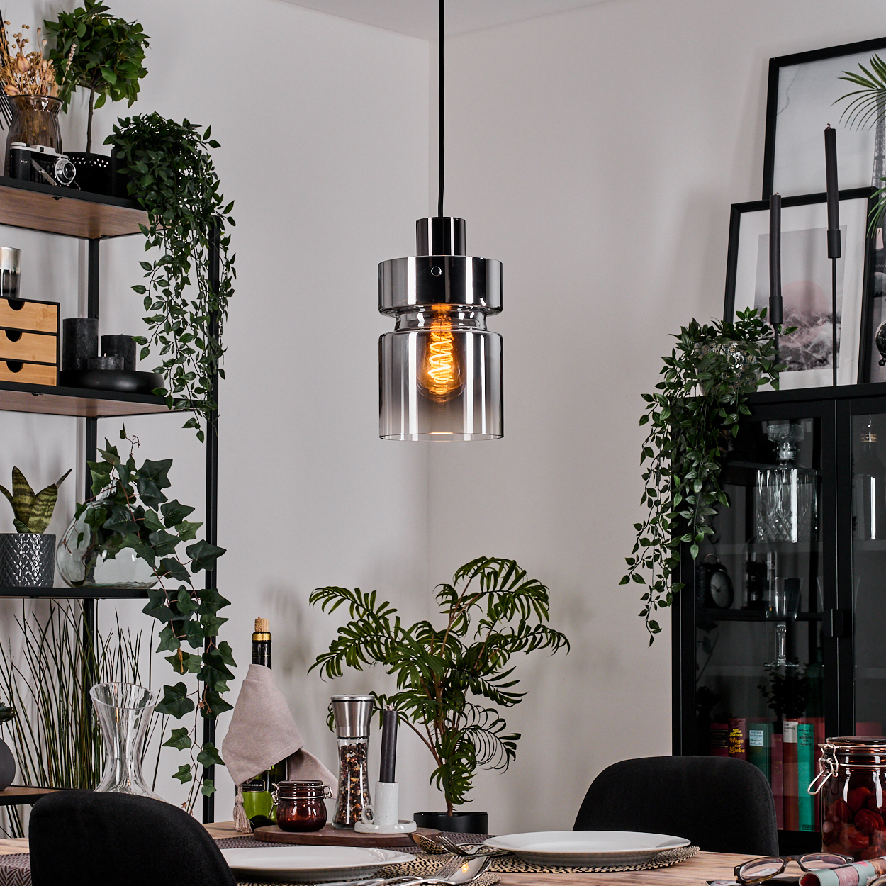 Ein modernes Esszimmer mit Hängelampe, gedecktem Tisch und dekorativen Pflanzen auf Regalen und Schränken.