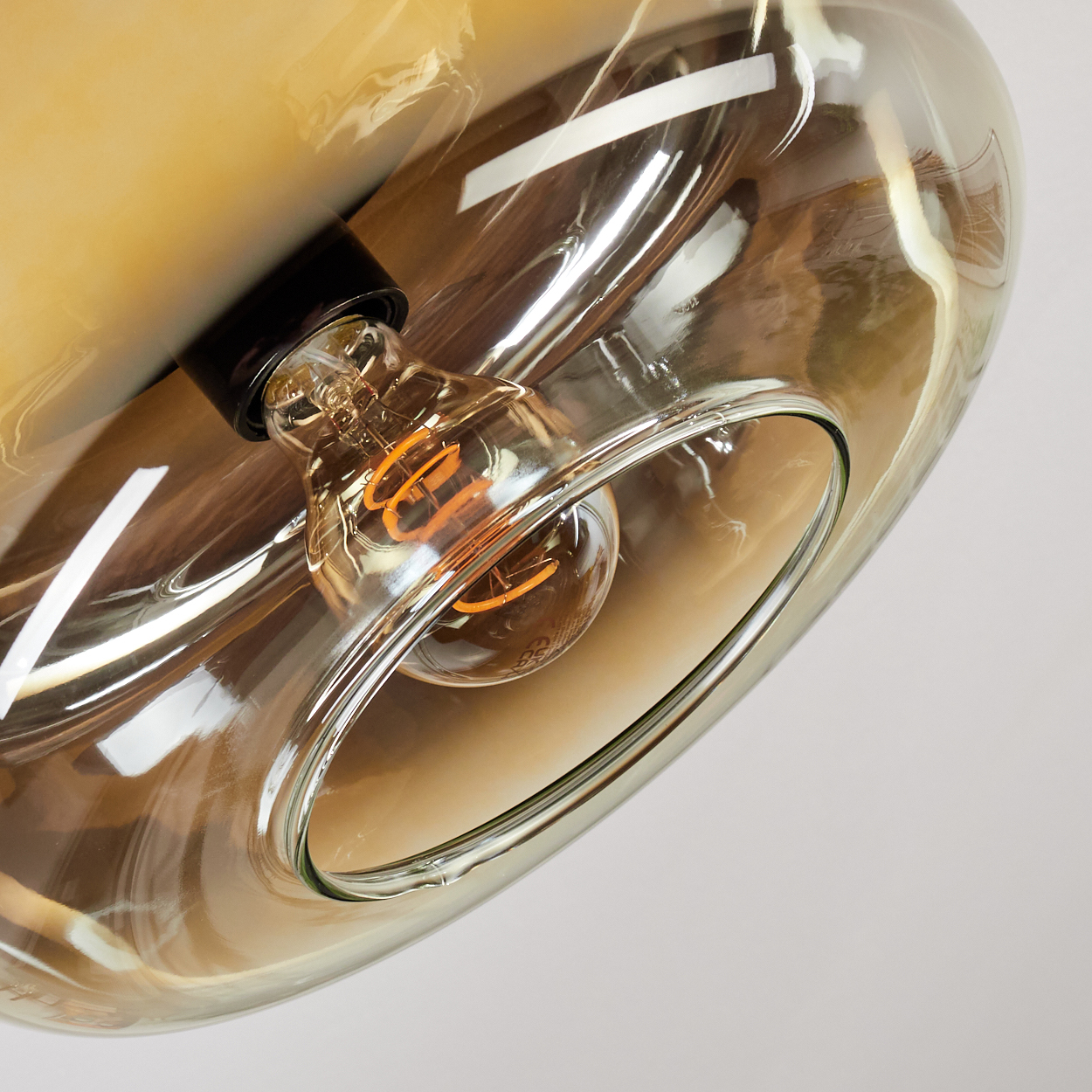 Nahaufnahme einer Glasleuchte. Eine brennende Glühbirne befindet sich in einem klaren, tropfenförmigen Glas. Das Glas hat eine bernsteinfarbene Tönung.