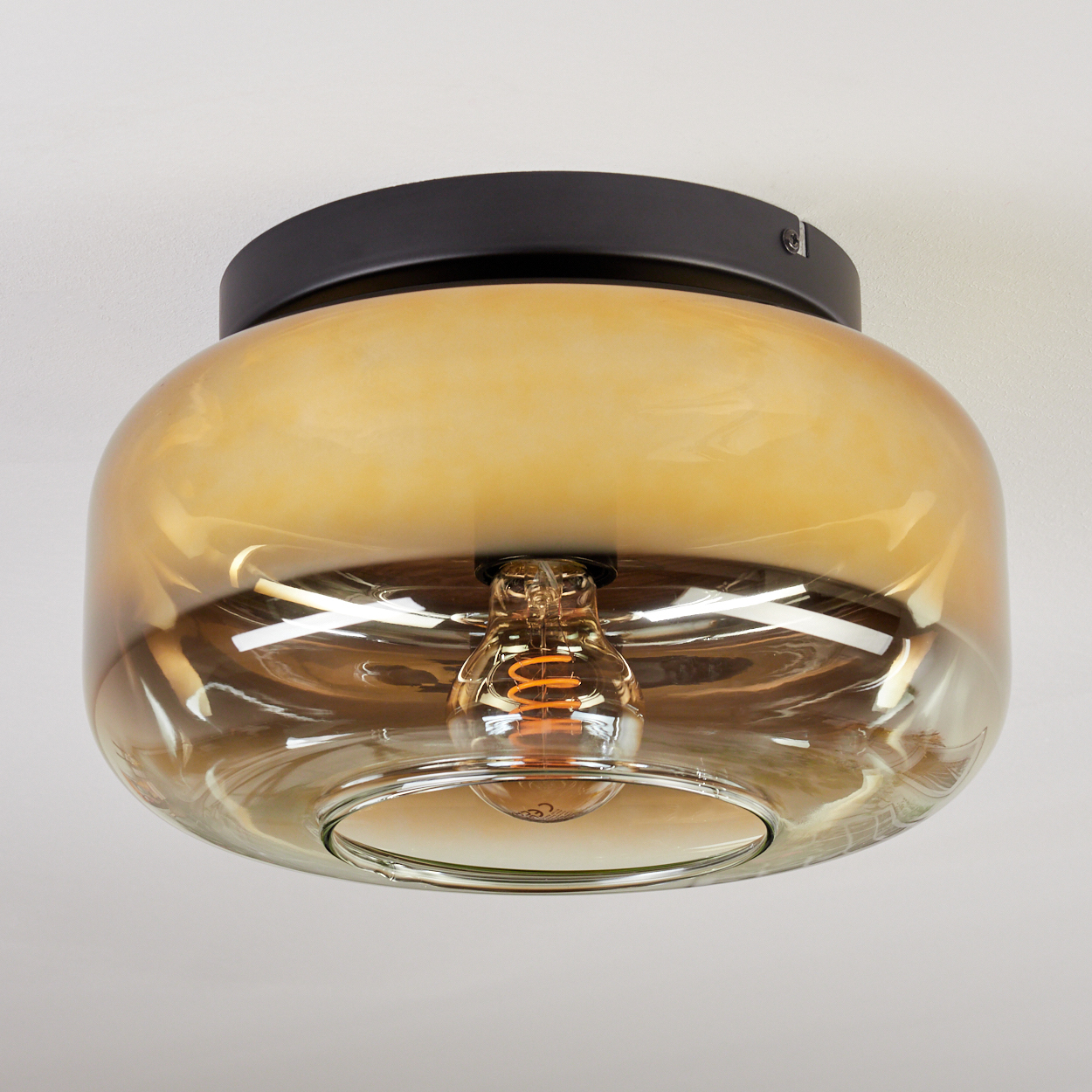 Eine moderne Deckenleuchte mit bernsteinfarbenem Glasschirm und sichtbarer Edison-Glühbirne. Die Leuchte ist an einer weißen Decke montiert.