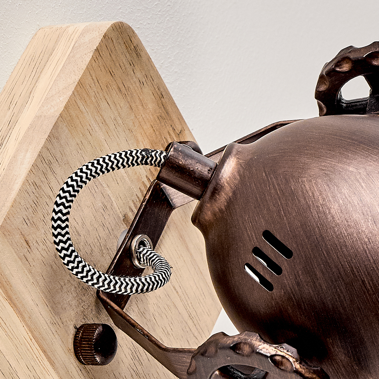 Nahaufnahme einer Wandlampe. Sie hat einen Holzsockel, einen bronzefarbenen Lampenschirm und ein schwarz-weißes Zickzack-Kabel.