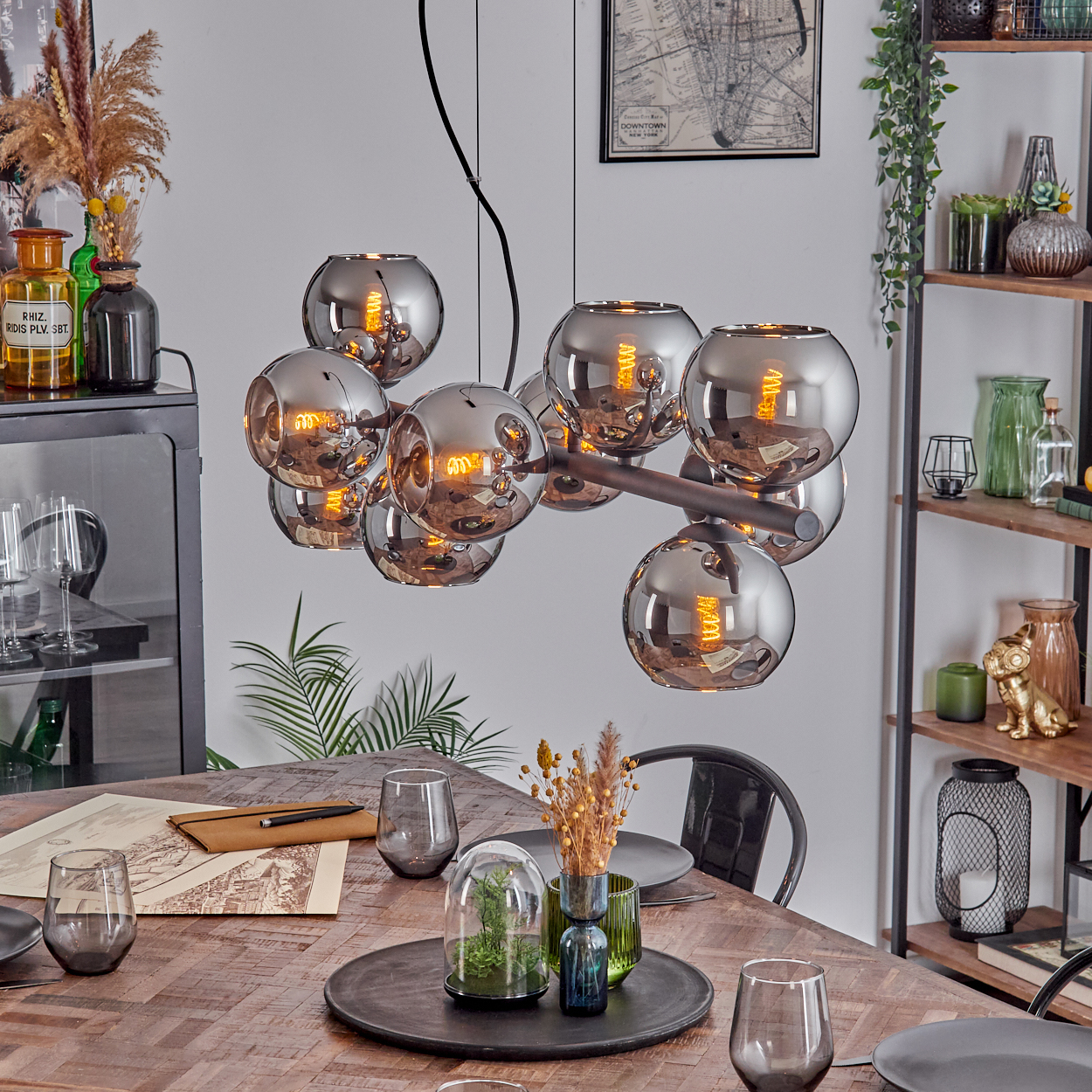 Esszimmer mit Holztisch, Gläsern und Kronleuchter mit Glaskugeln. Deko-Artikel stehen auf einem Regal.