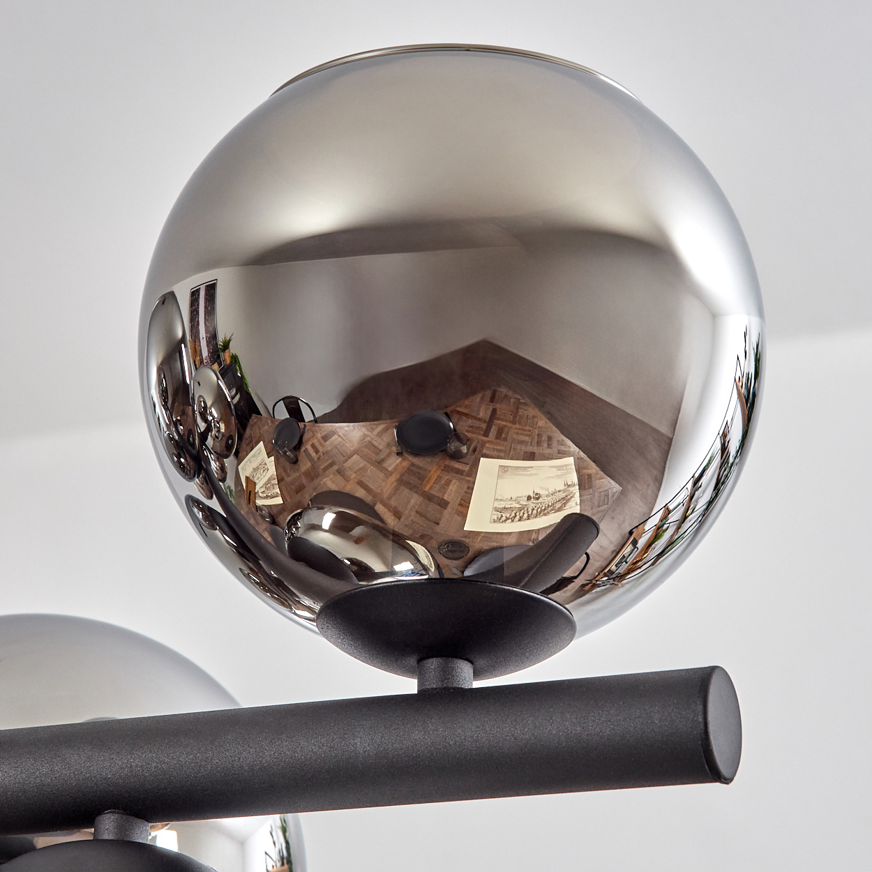 Eine verchromte Kugel spiegelt einen Raum mit Holzboden, Möbeln und Kunst wider. Es ist Teil einer schwarzen Metallleuchte.