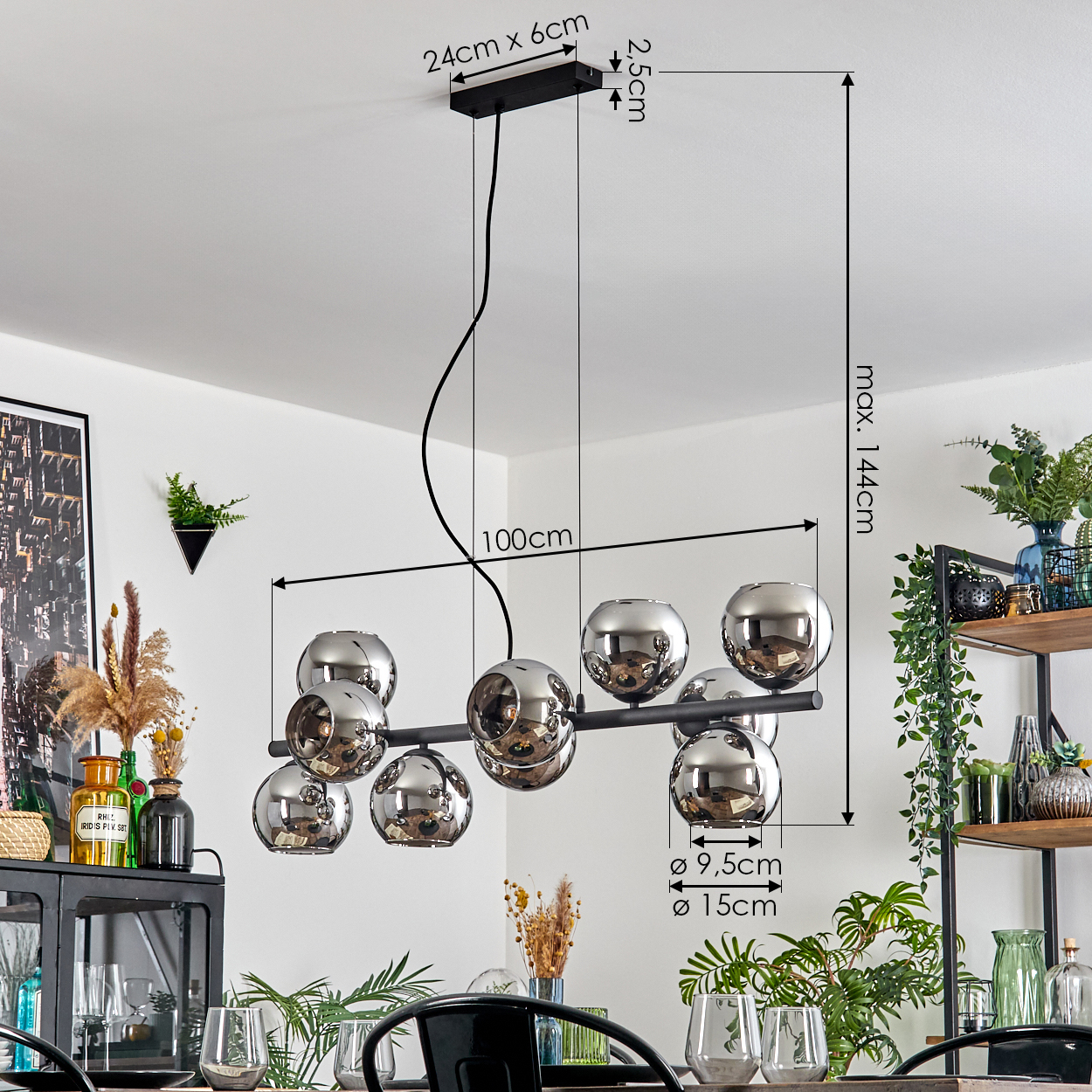 Eine moderne Hängelampe mit kugelförmigen Lichtern hängt von der Decke. Ein Tisch und Pflanzen sind im Vorder- und Hintergrund zu sehen.