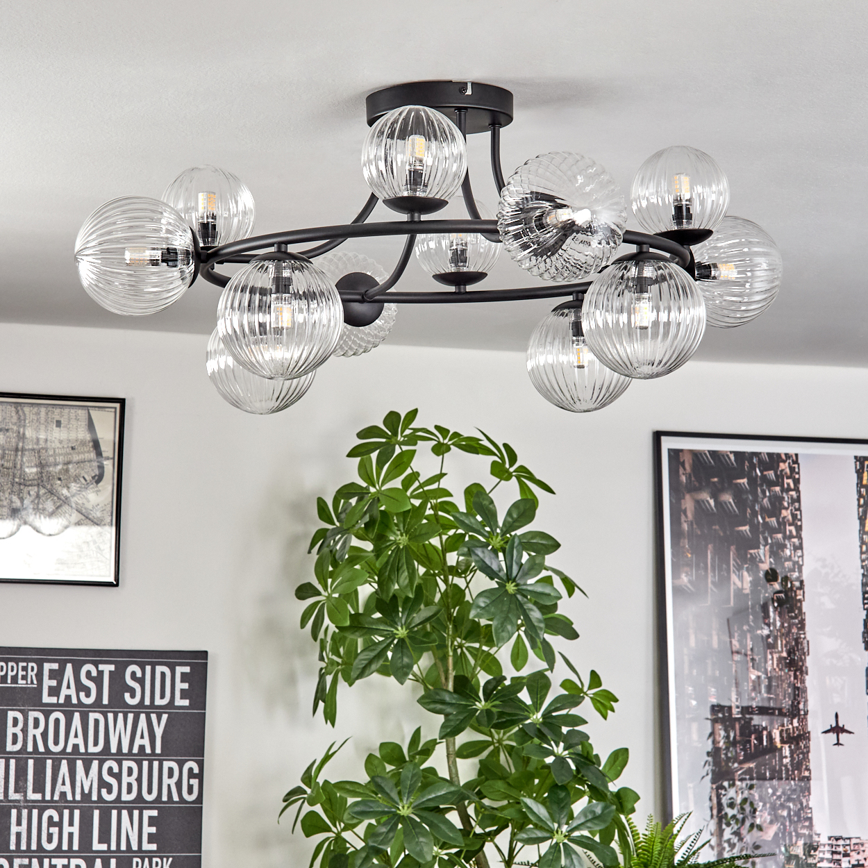 Eine moderne Deckenleuchte mit Glaskugeln hängt von der Decke. Im Vordergrund befindet sich eine Pflanze, an der Wand gerahmte Kunst.