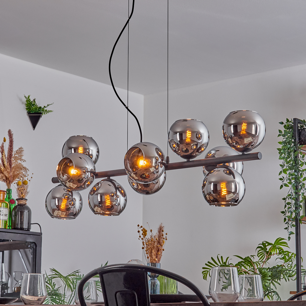 Ein modernes Esszimmer mit einem Kronleuchter mit kugelförmigen Lichtern. Der Tisch ist mit Gläsern und einem schwarzen Stuhl gedeckt.