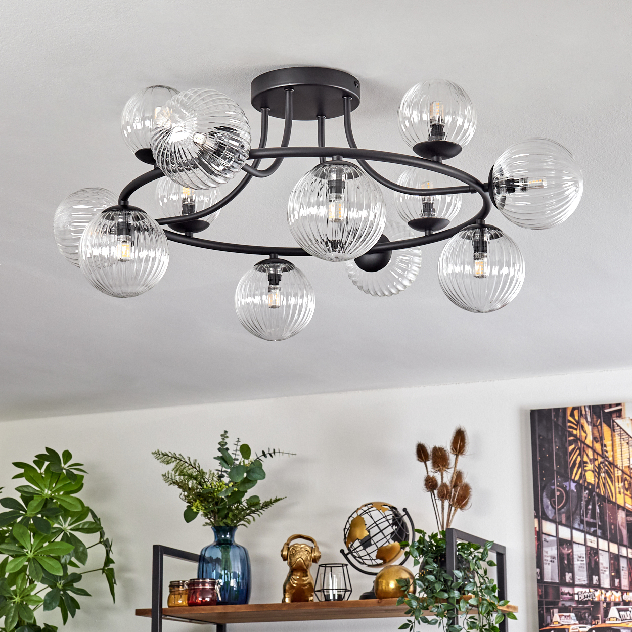 Eine moderne Deckenleuchte mit Glaskugeln hängt über einem Regal mit Dekoration. Das Regal enthält Pflanzen, einen Globus und eine goldene Hundestatue.