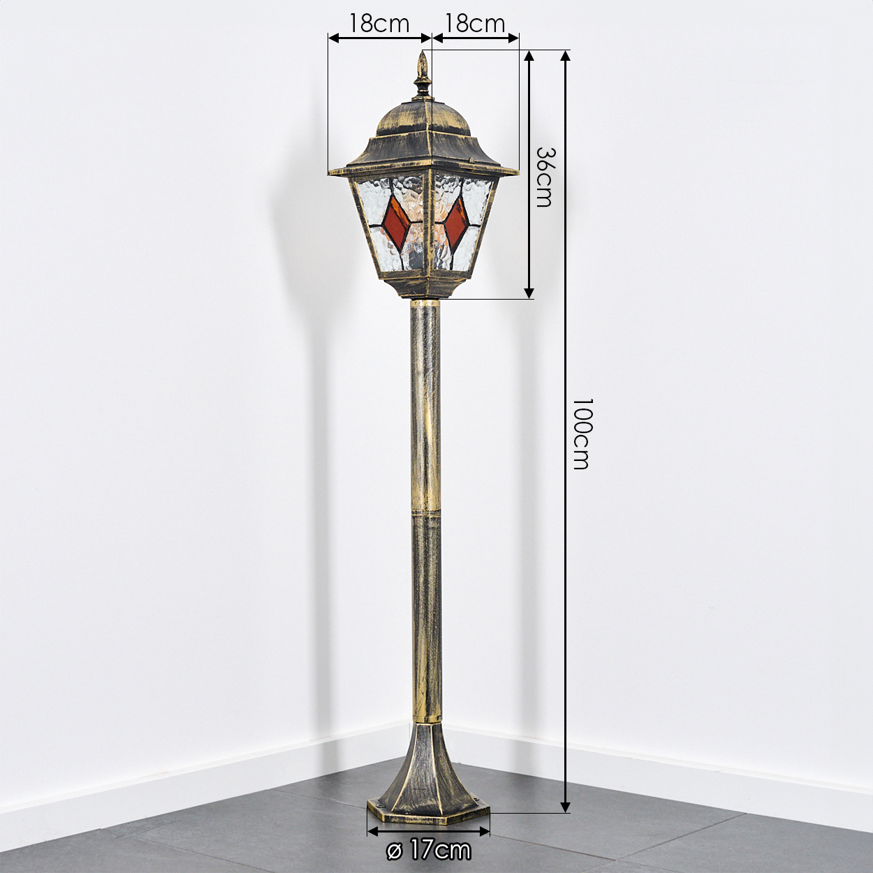 Eine bronzefarbene Außenlampe steht auf einem grauen Fliesenboden vor einer weißen Wand. Abmessungen sind angegeben.