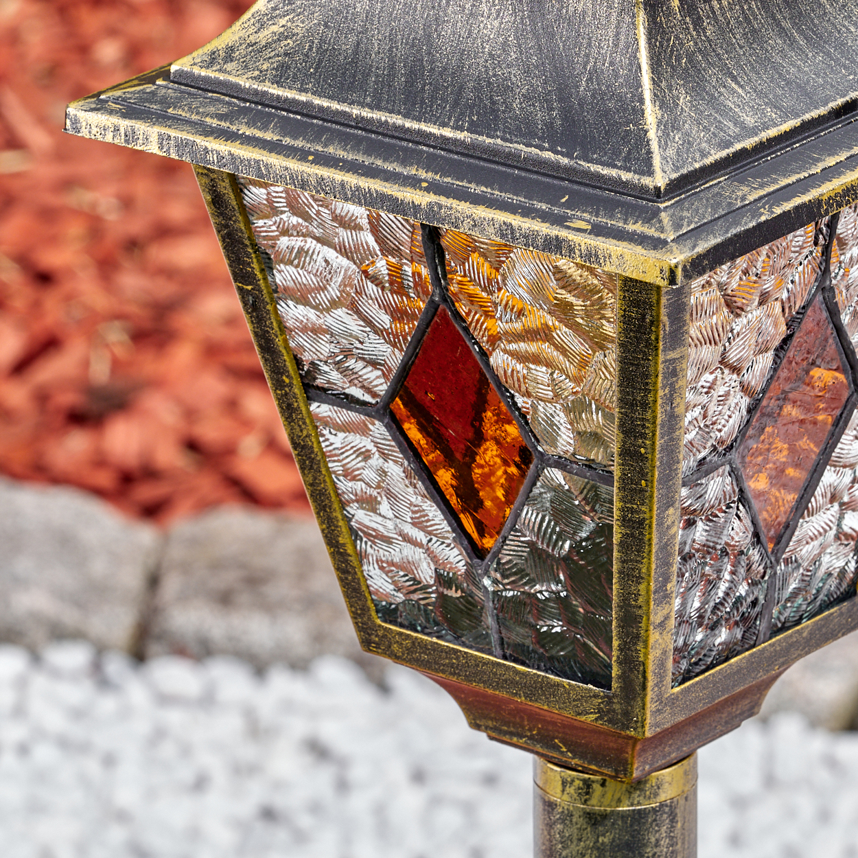 Nahaufnahme einer dekorativen Außenlampe. Sie hat einen Bronzerahmen, Buntglasscheiben mit roten und orangefarbenen Rauten.
