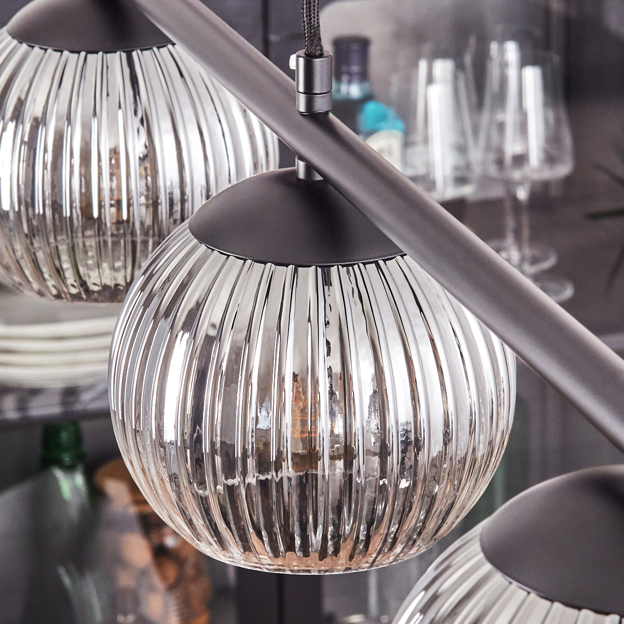 Nahaufnahme einer modernen Deckenleuchte mit drei kugelförmigen, geriffelten Glasschirmen. Der Metallrahmen und die Schirme sind silber und schwarz.