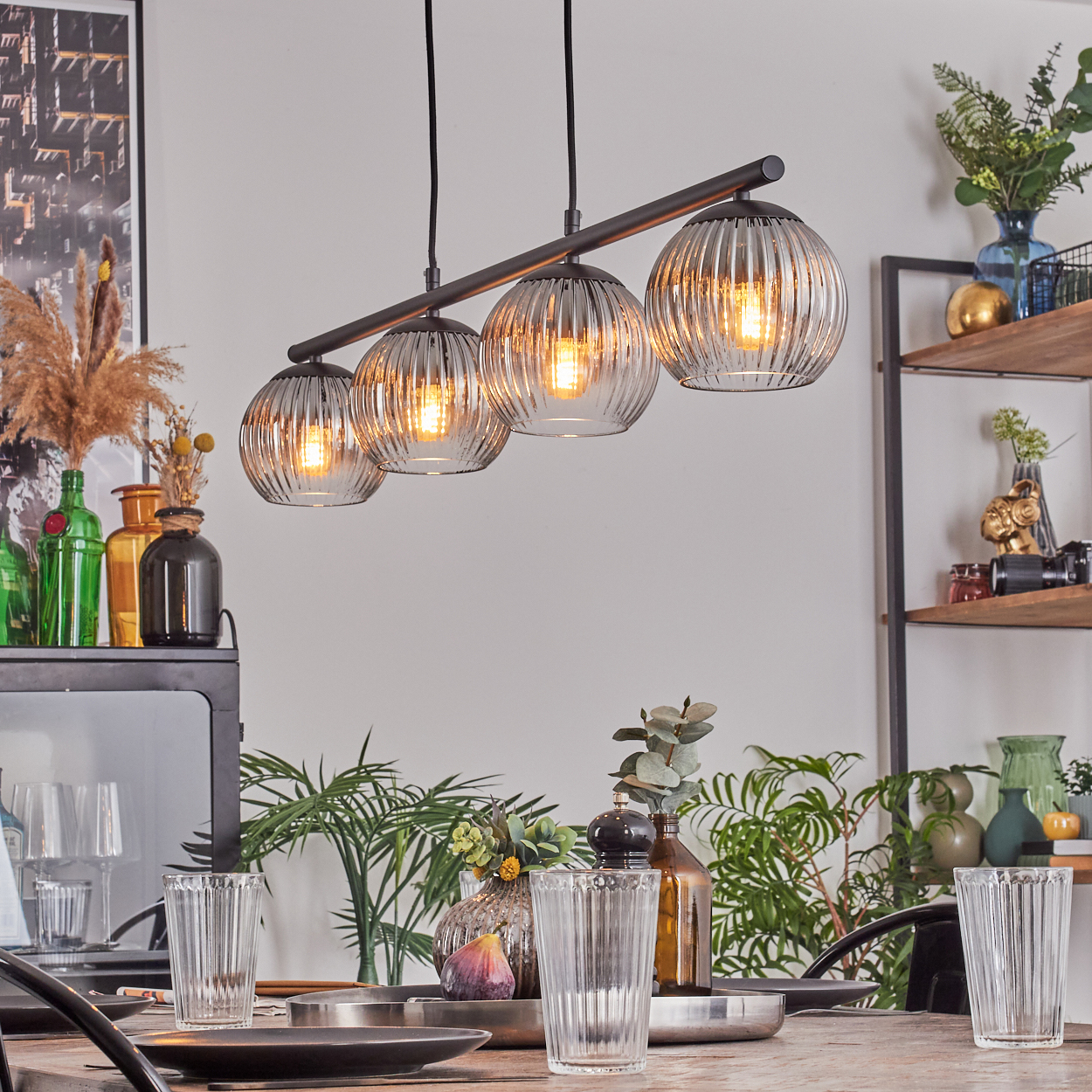 Ein Esszimmer zeigt eine Hängelampe mit vier Glaskugeln, einen Holztisch und verschiedene Dekorationsgegenstände.