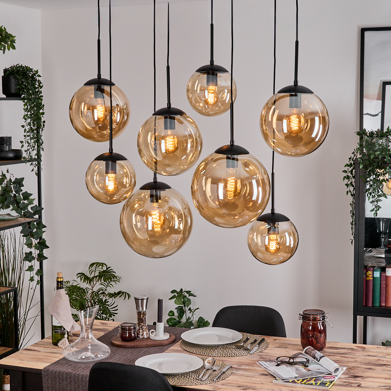 Esszimmer mit acht kugelförmigen Pendelleuchten. Holztisch mit Tellern und Gläsern. Pflanzen und Regale im Hintergrund.