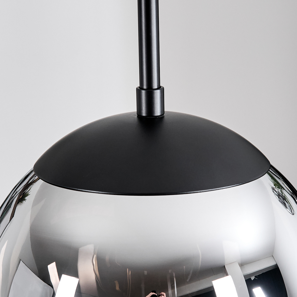 Eine moderne Pendelleuchte mit silberfarbenem, reflektierendem Glasschirm und schwarzem Oberteil und Stiel vor weißem Hintergrund.