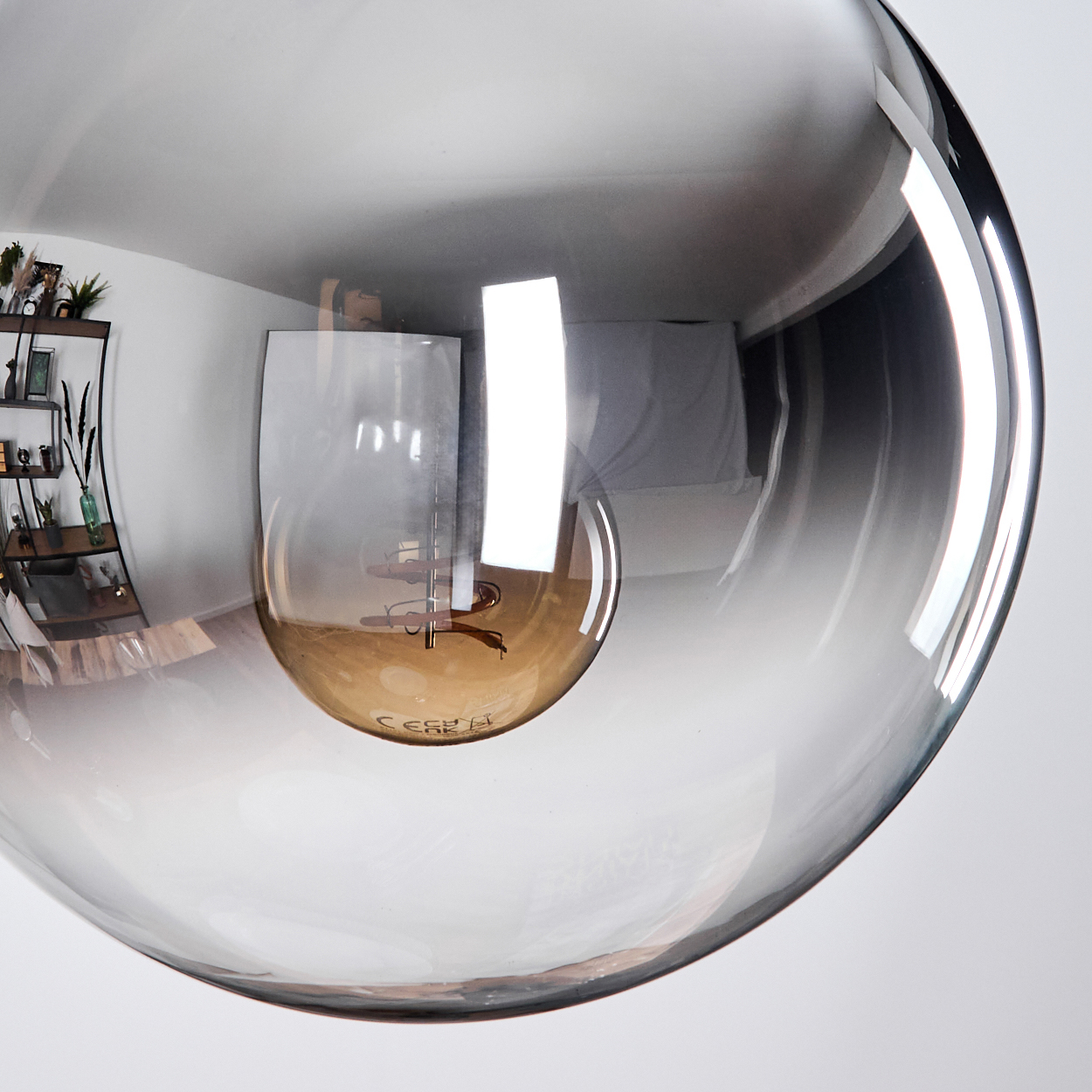 Nahaufnahme einer großen, klaren Glasleuchte mit einer braunen Glühbirne im Inneren. Die Glühbirne reflektiert den Raum.
