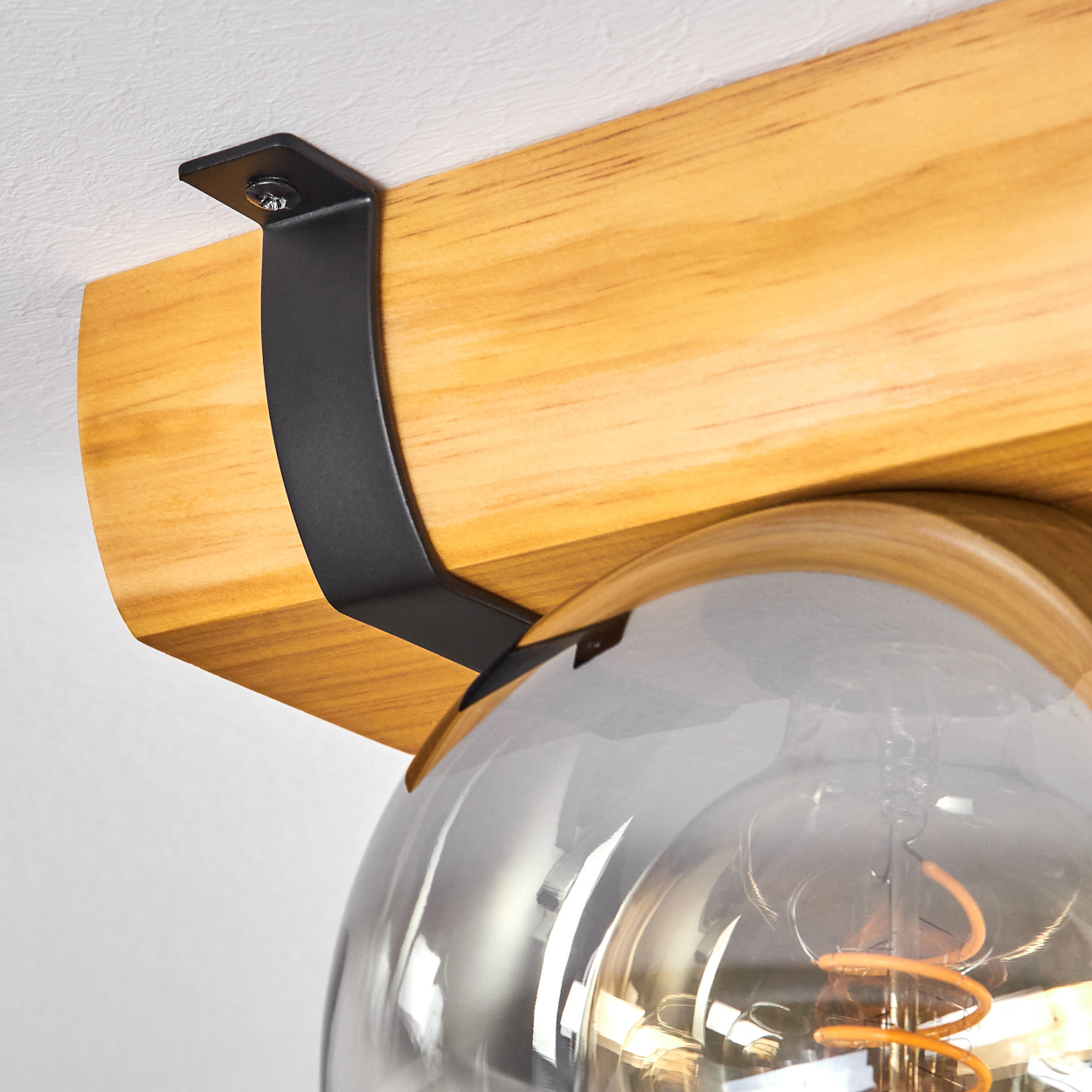 Nahaufnahme eines Holzbalkens mit einer schwarzen Metallhalterung. Darunter eine klare Glühbirne. Der Hintergrund ist eine weiße Decke.