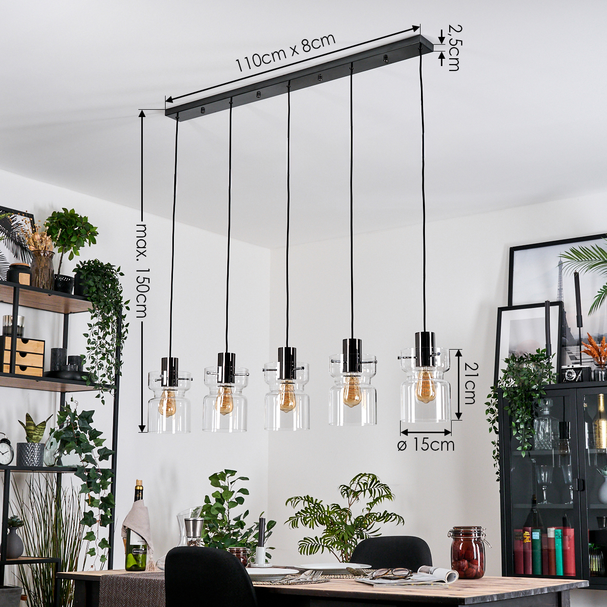Ein Esszimmer mit schwarzer Leuchte mit fünf Glühbirnen, Pflanzen, einem Tisch und einem schwarzen Schrank mit Büchern und Dekorationen.