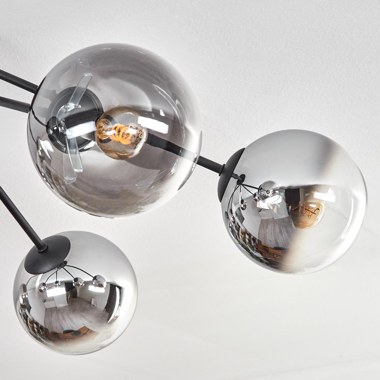 Eine moderne Deckenleuchte mit drei kugelförmigen Glasschirmen, die den Raum widerspiegeln. Schwarze Stäbe verbinden die Schirme mit der Decke.