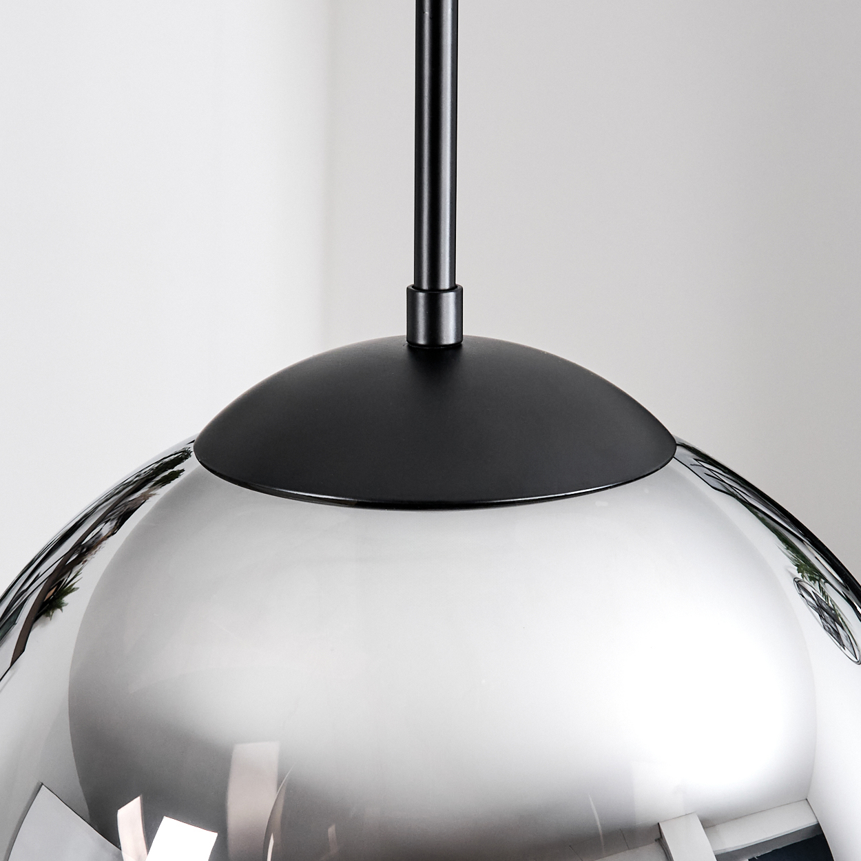 Eine moderne Pendelleuchte mit silberfarbenem, reflektierendem Schirm und schwarzem Oberteil. Die Leuchte hängt an einer schwarzen Stange.