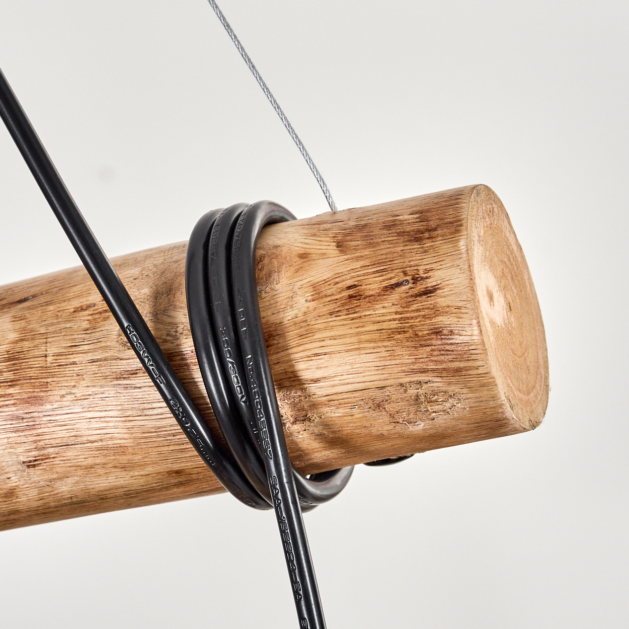 Ein Holzstamm mit einem schwarzen Kabel, das darum gewickelt ist, und einem dünnen Draht darüber, vor weißem Hintergrund.