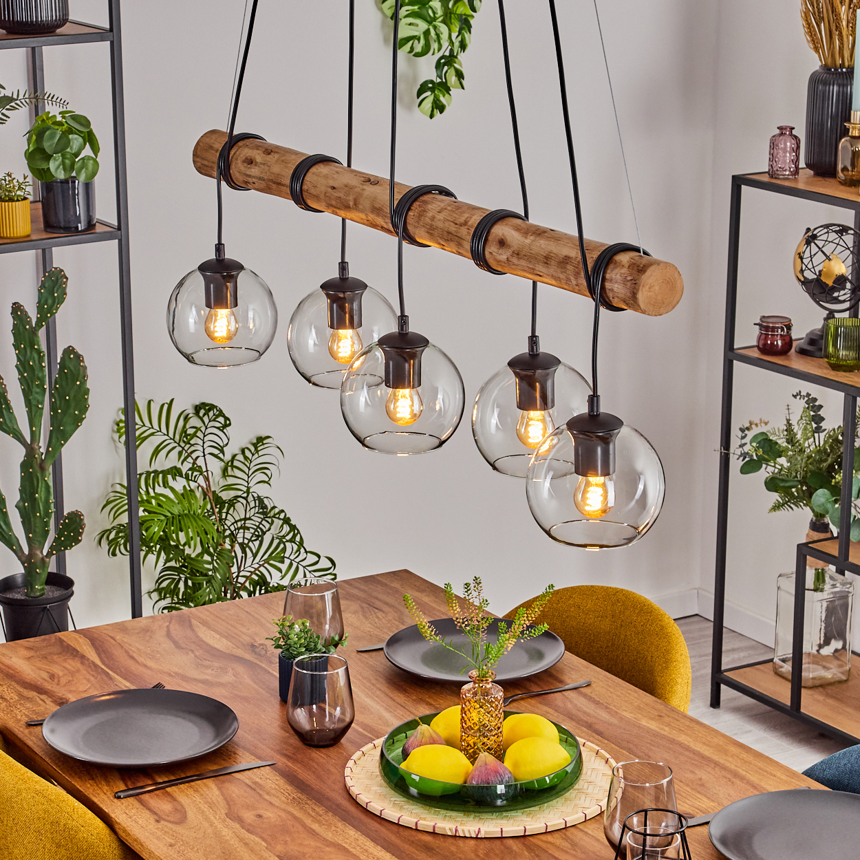 Esszimmer mit Holztisch, Glaslampen und Holzbalken. Auf dem Tisch stehen Teller, Gläser und Pflanzen.