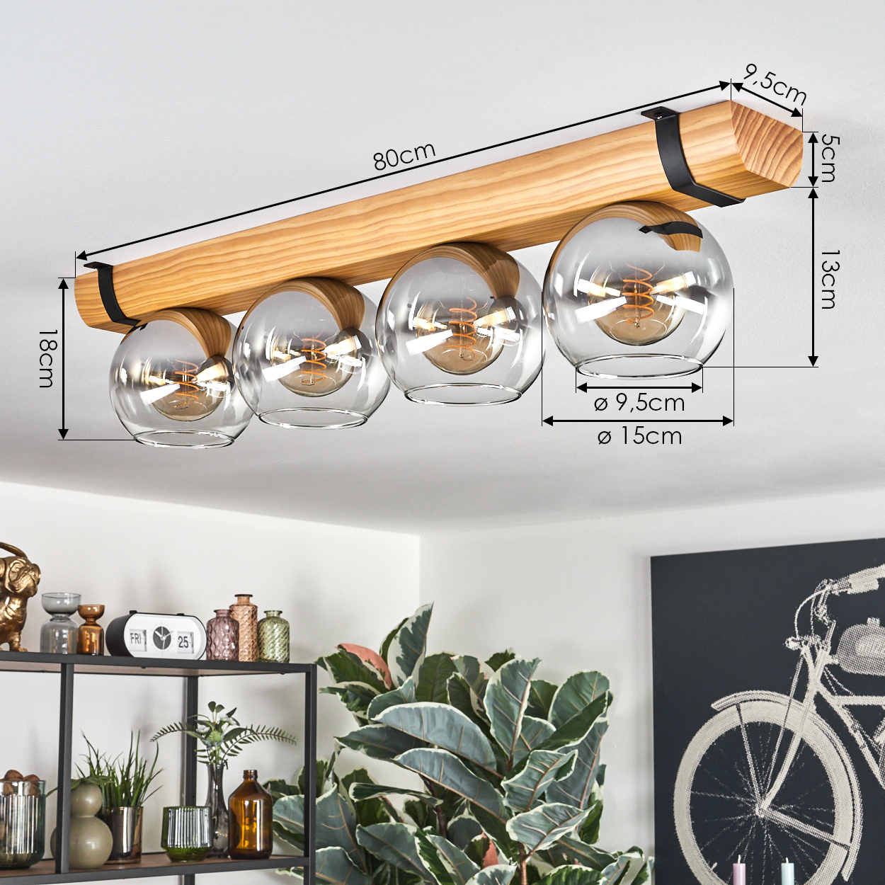 Eine Deckenleuchte aus Holz mit vier Glaskugeln. Maße sind angegeben. Im Hintergrund ein Regal und ein Fahrradkunstwerk.
