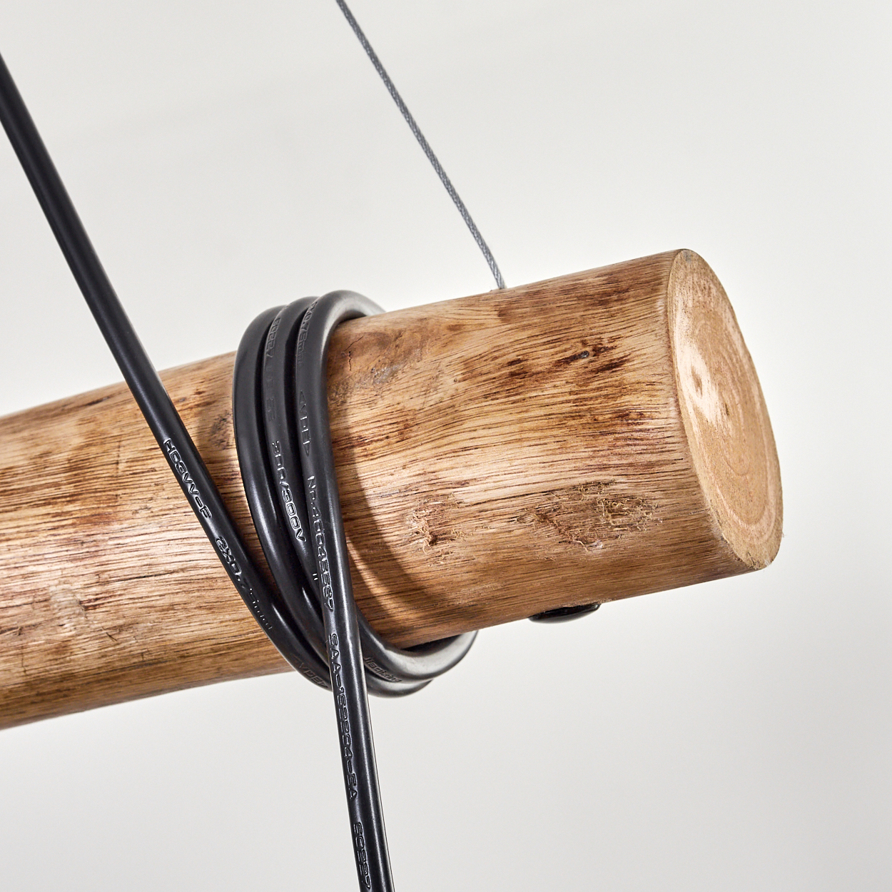 Ein Holzstamm mit schwarzen Kabeln. Ein grauer Draht hängt von oben. Weißer Hintergrund.