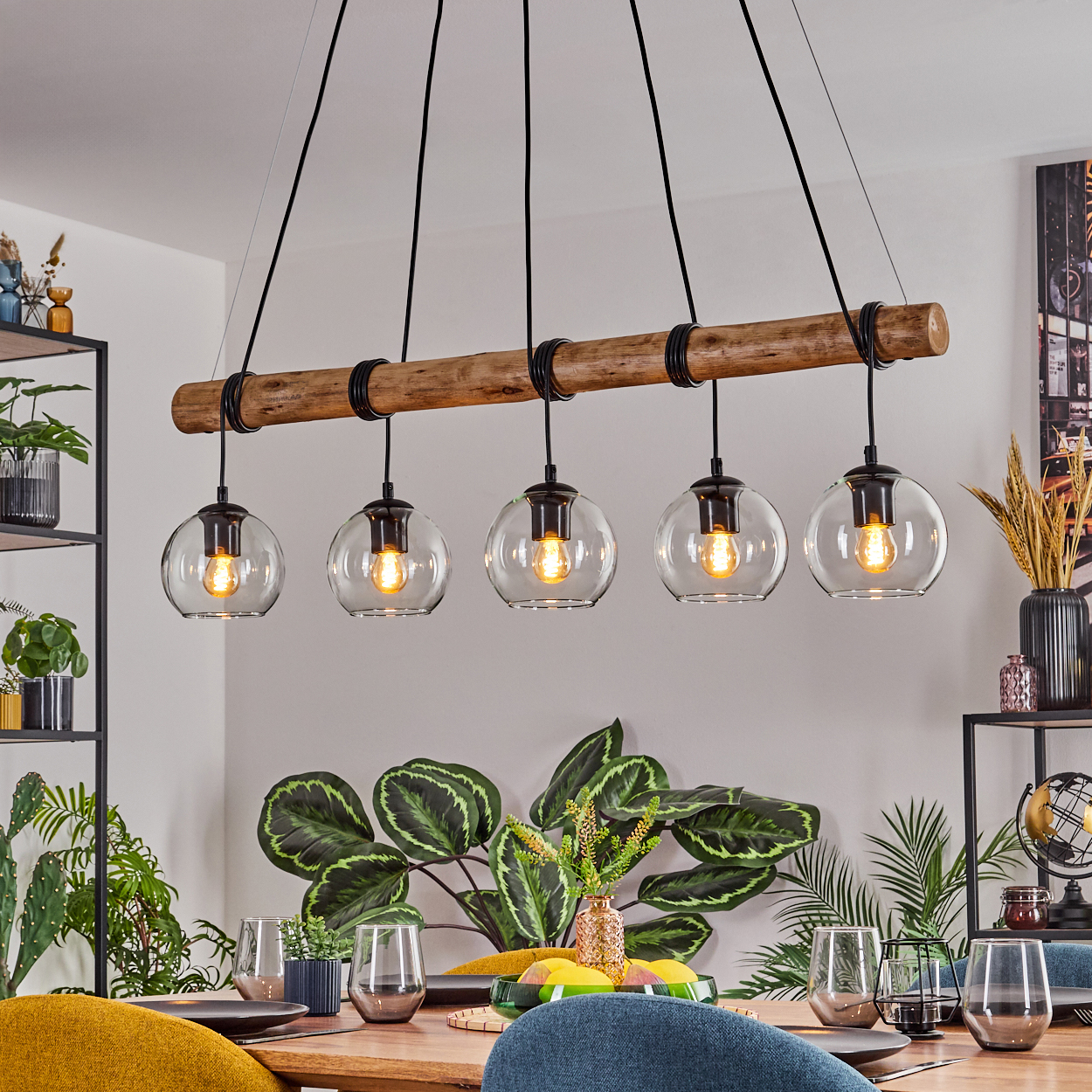 Ein Esszimmer mit Holztisch, moderner Kronleuchter mit fünf Glaskugeln und Pflanzen.