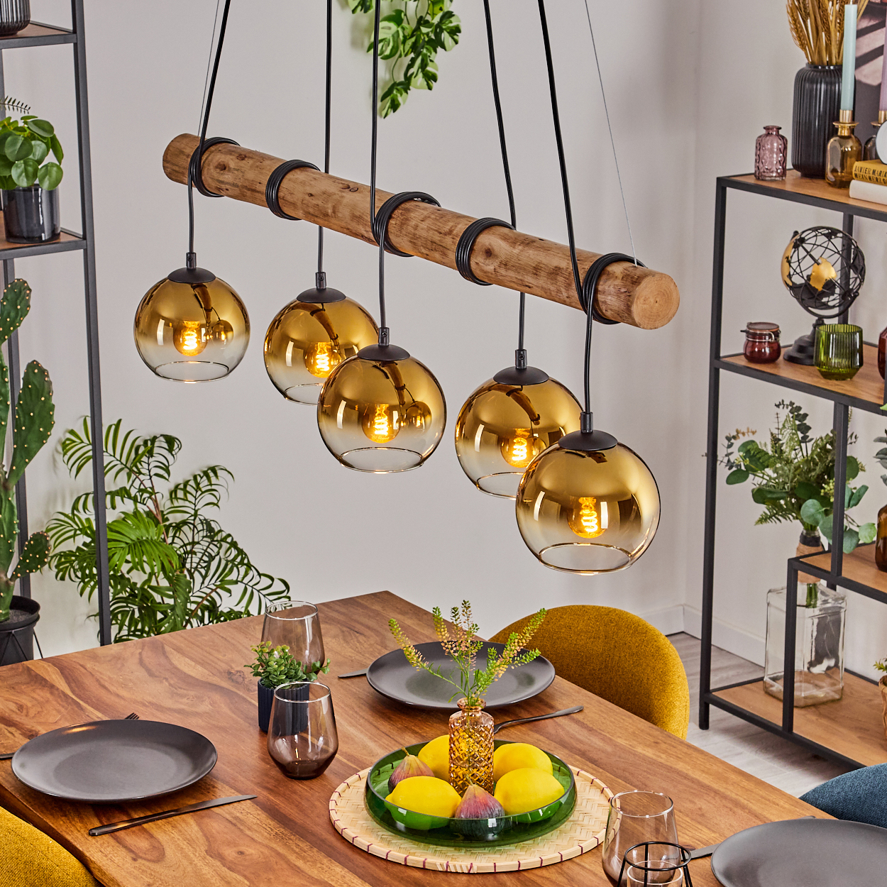 Esszimmer mit Holztisch und Hängeleuchten. Tisch gedeckt mit Tellern, Gläsern und einer Obstplatte. Bücherregale im Hintergrund.