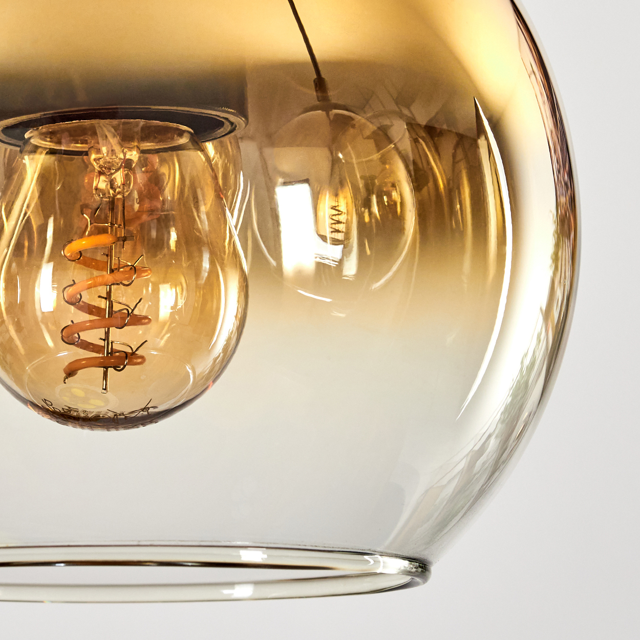 Nahaufnahme einer Glasleuchte mit einer Glühbirne mit Spiralfaden in einem runden, bernsteinfarbenen Glasschirm.
