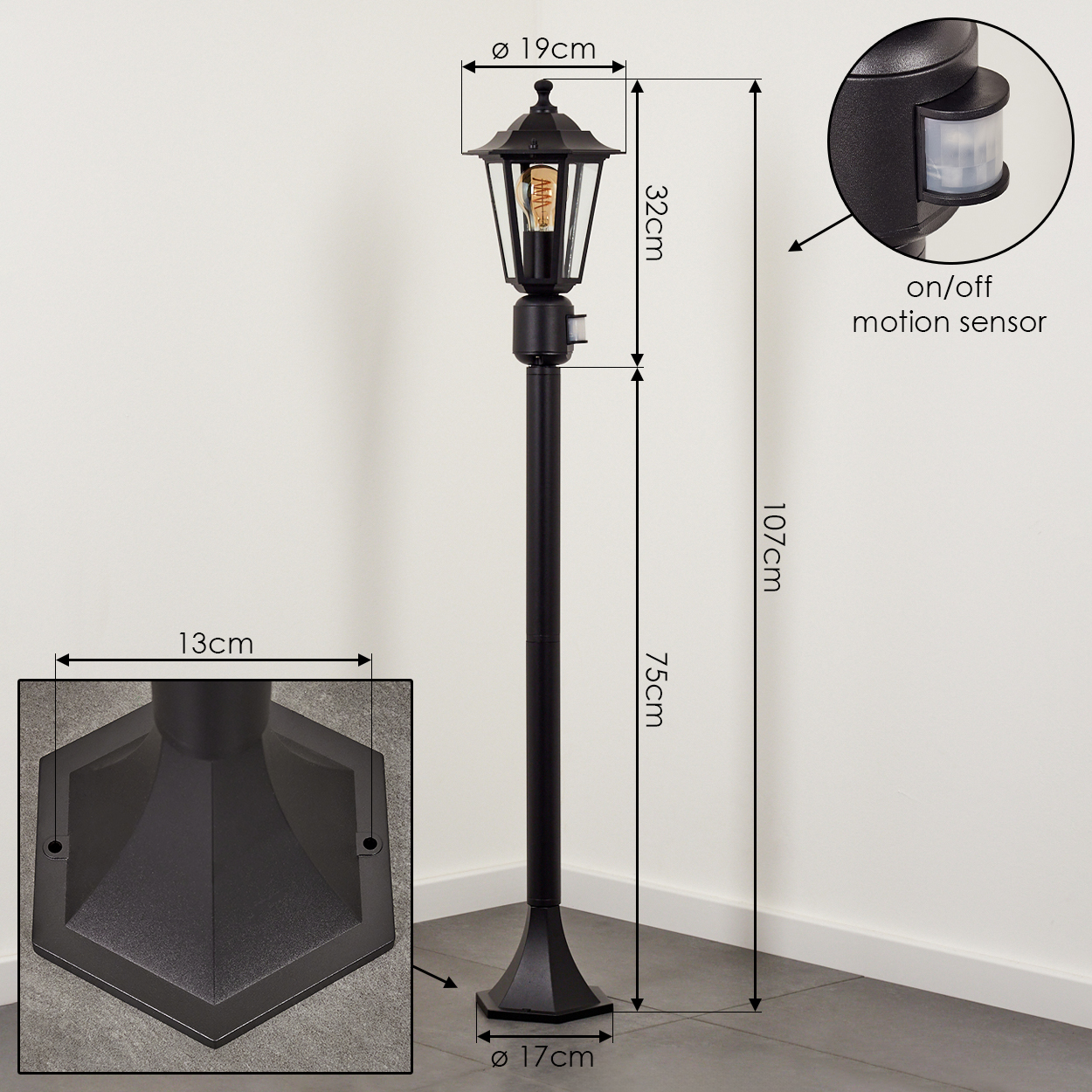 Schwarze Außenlampe mit Bewegungsmelder. Die Lampe hat ein klassisches Design und steht auf einem Fliesenboden neben einer weißen Wand.