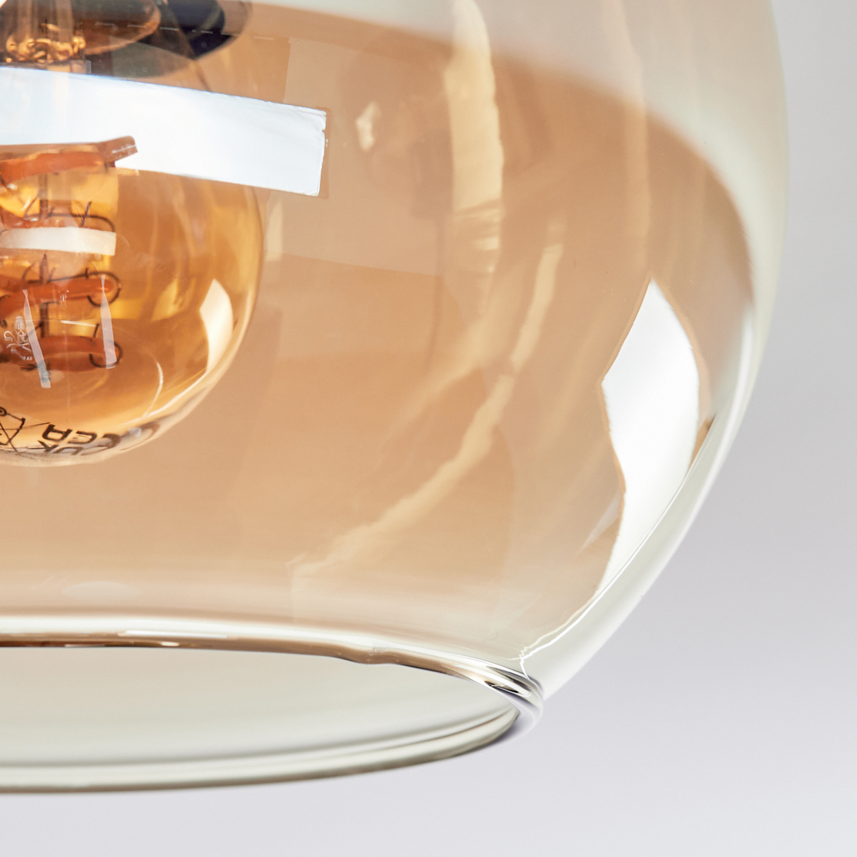Nahaufnahme eines Glasschirms mit Glühbirne. Der Schirm ist bernsteinfarben, die Glühbirne leuchtet.