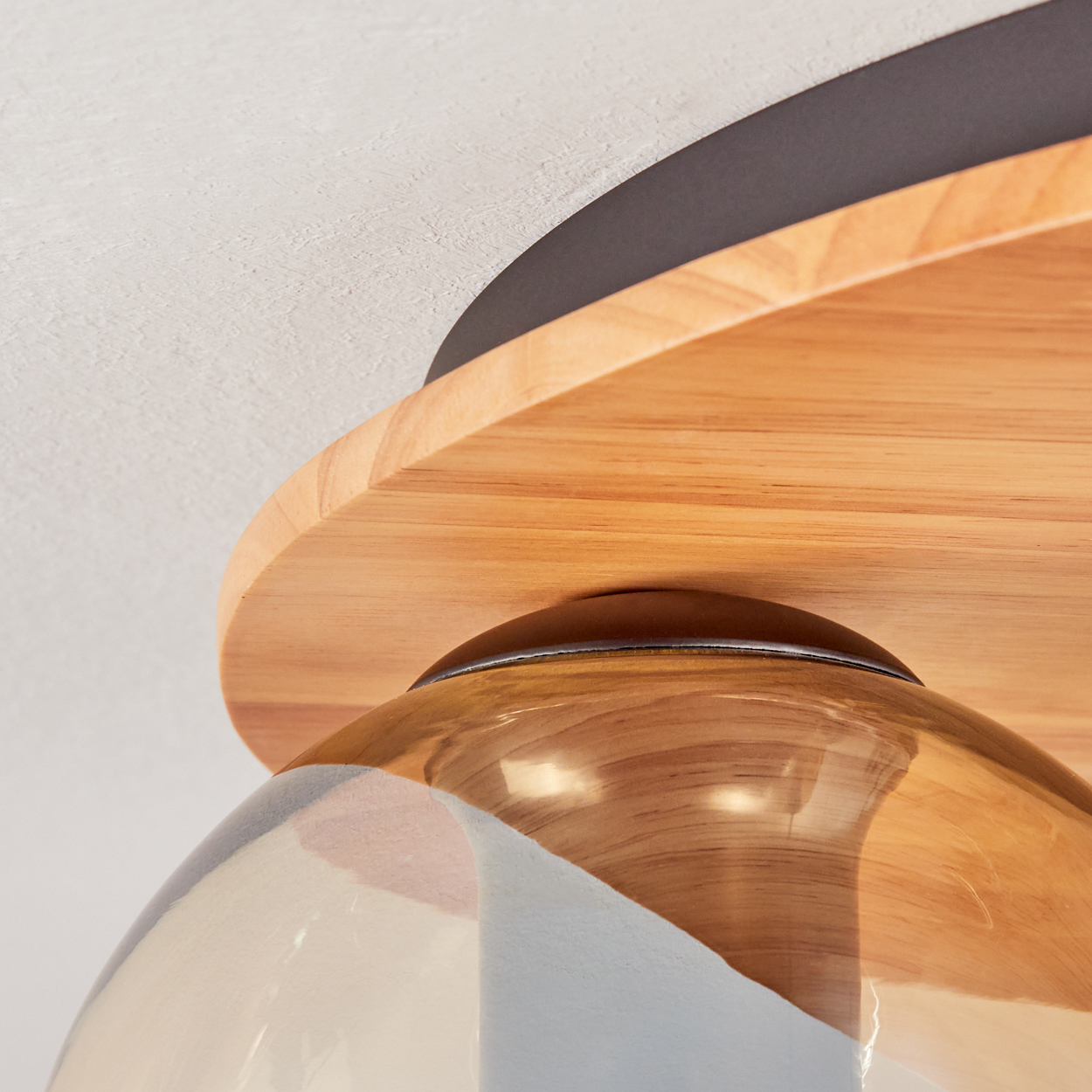 Nahaufnahme einer Holzdeckenleuchte. Sie hat einen Holzschirm, dunkle Metallverkleidung und einen klaren, glockenförmigen Glasdiffusor.