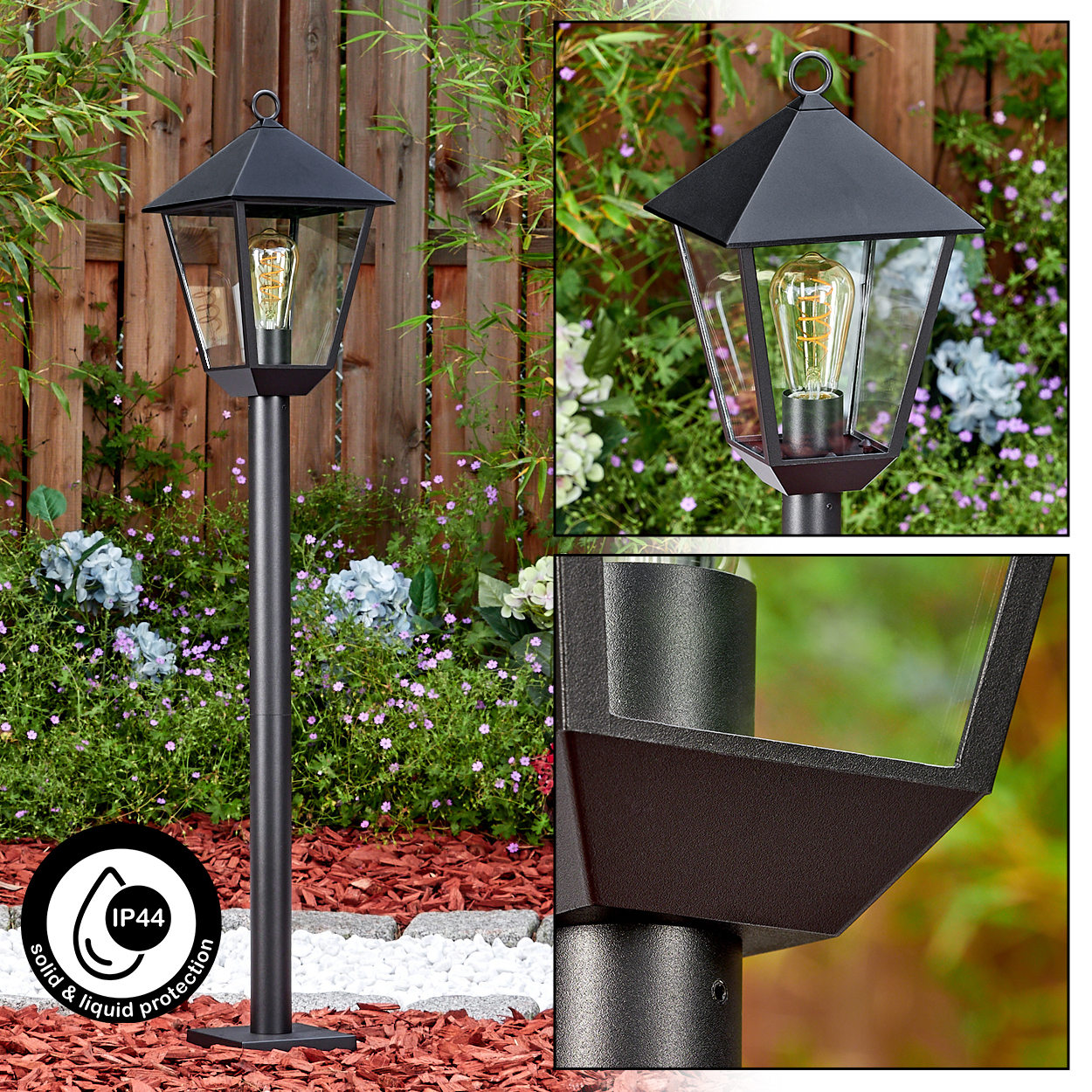 Eine schwarze Außenlampe mit Glasgehäuse, die auf einer schwarzen Stange steht. Im Hintergrund ein Holzzaun und Blumen.