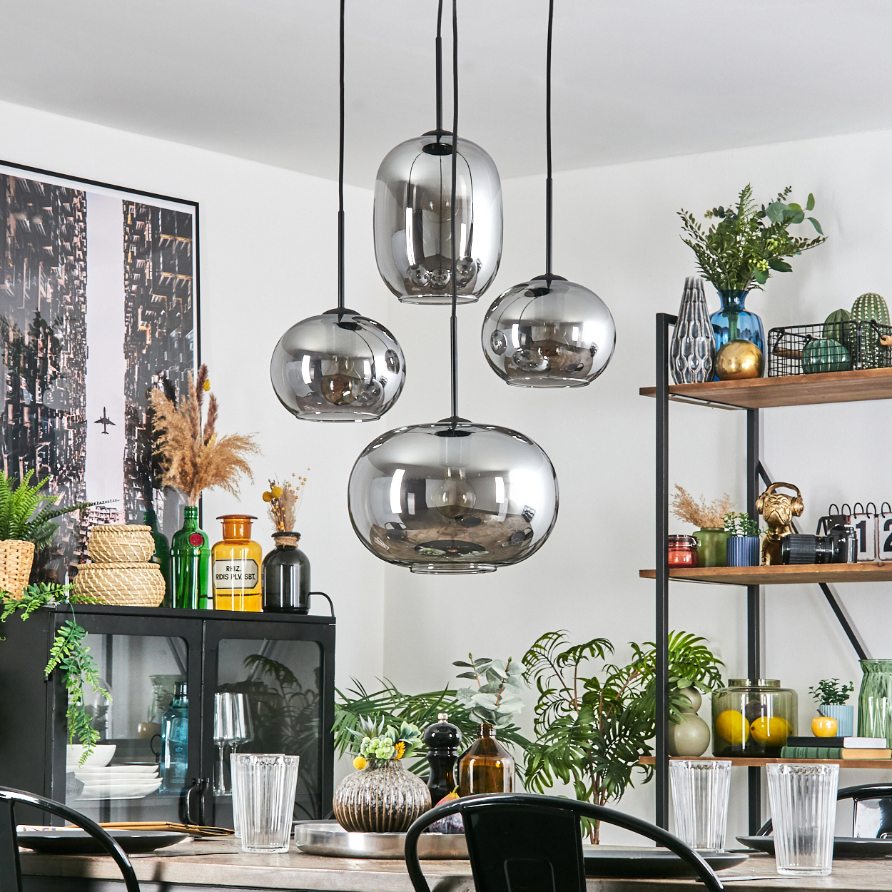 Esszimmer mit Hängelampen, einem gedeckten Tisch und Dekorationsgegenständen auf Regalen und Schränken, mit Pflanzen.