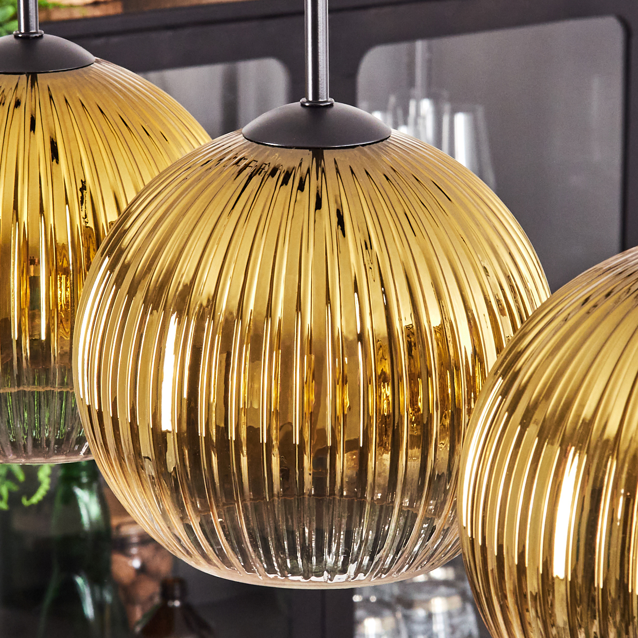 Nahaufnahme von drei goldenen, gerippten Glas-Pendelleuchten. Jede hat eine schwarze Kappe und hängt von der Decke. Ein dunkler Hintergrund ist sichtbar.