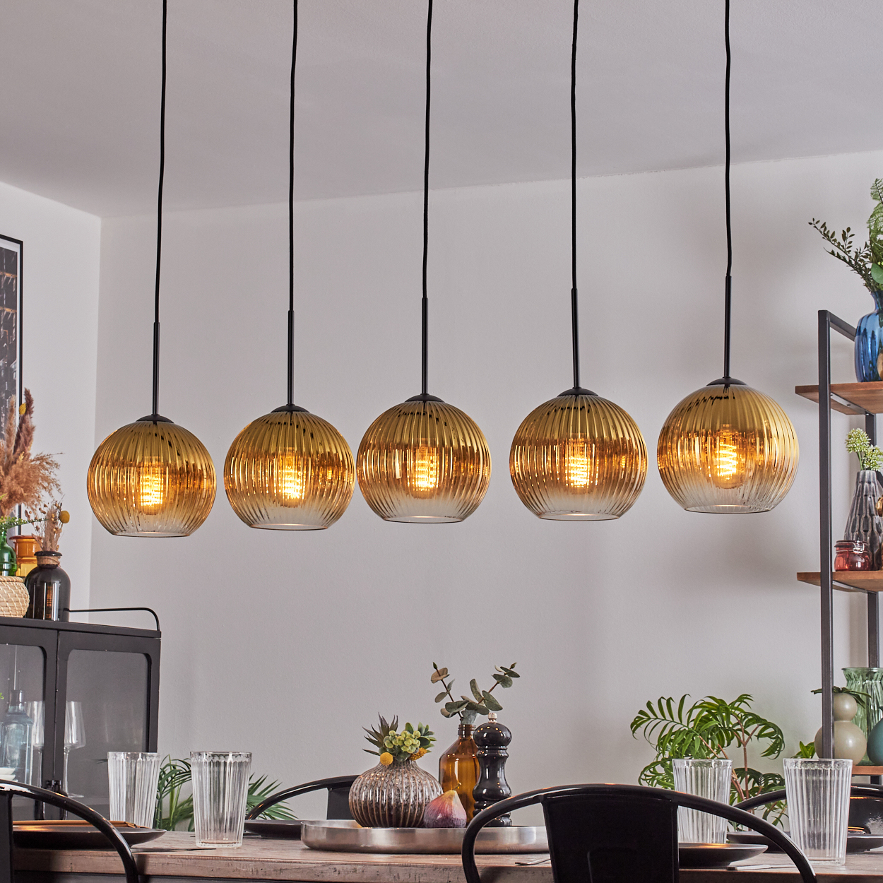 Fünf goldene Pendelleuchten über einem Esstisch. Pflanzen und Dekorationen auf dem Tisch und im Hintergrund.