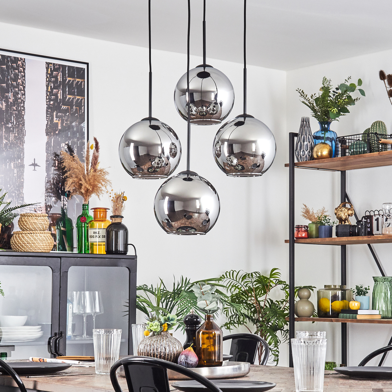 Esszimmer mit vier Chrom-Kugel-Pendelleuchten. Tisch mit Tellern und Gläsern. Regale mit Dekorationen im Hintergrund.