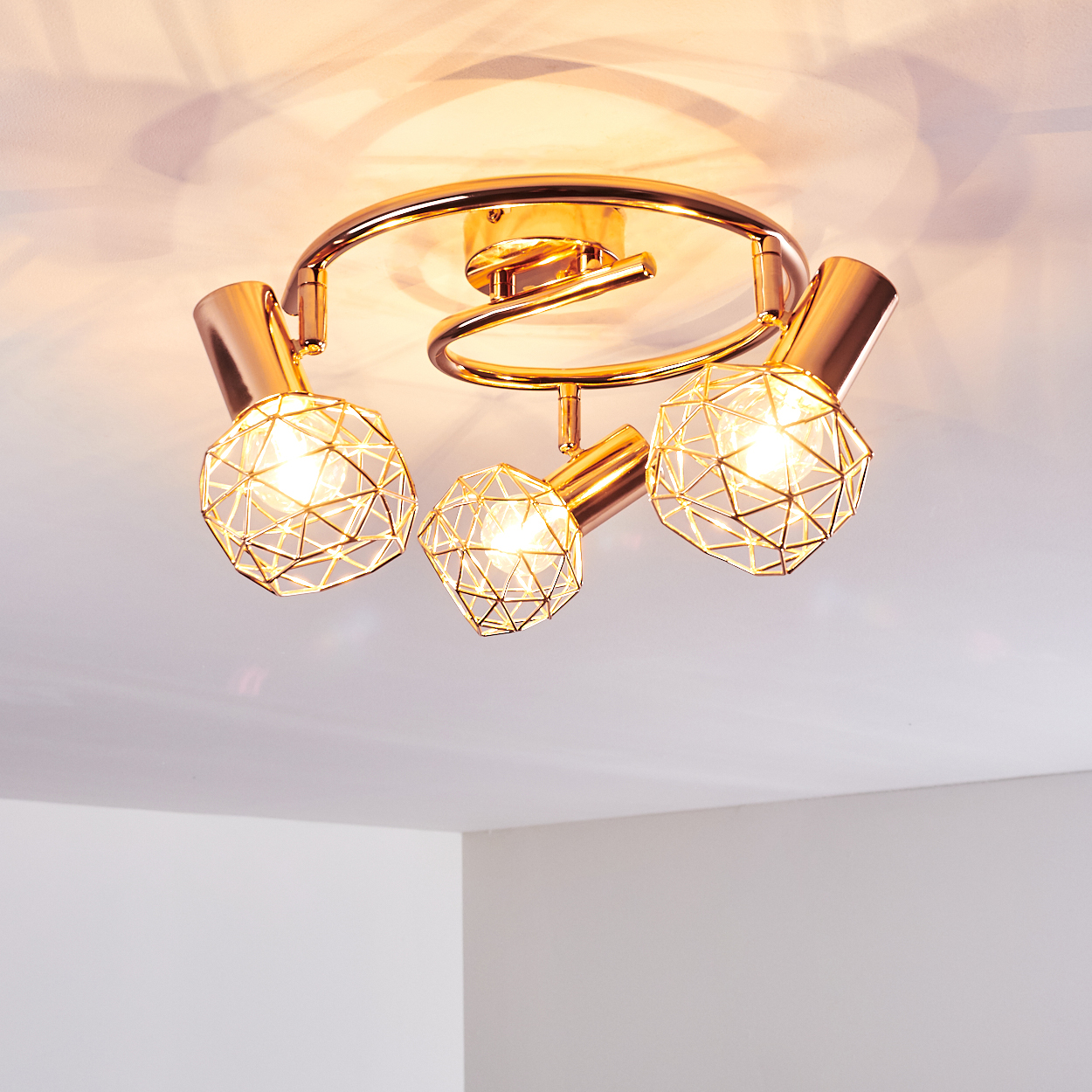 Moderne Deckenleuchte mit drei goldfarbenen Lampenschirmen, jedes mit geometrischem Drahtrahmen-Design, vor weißer Decke.