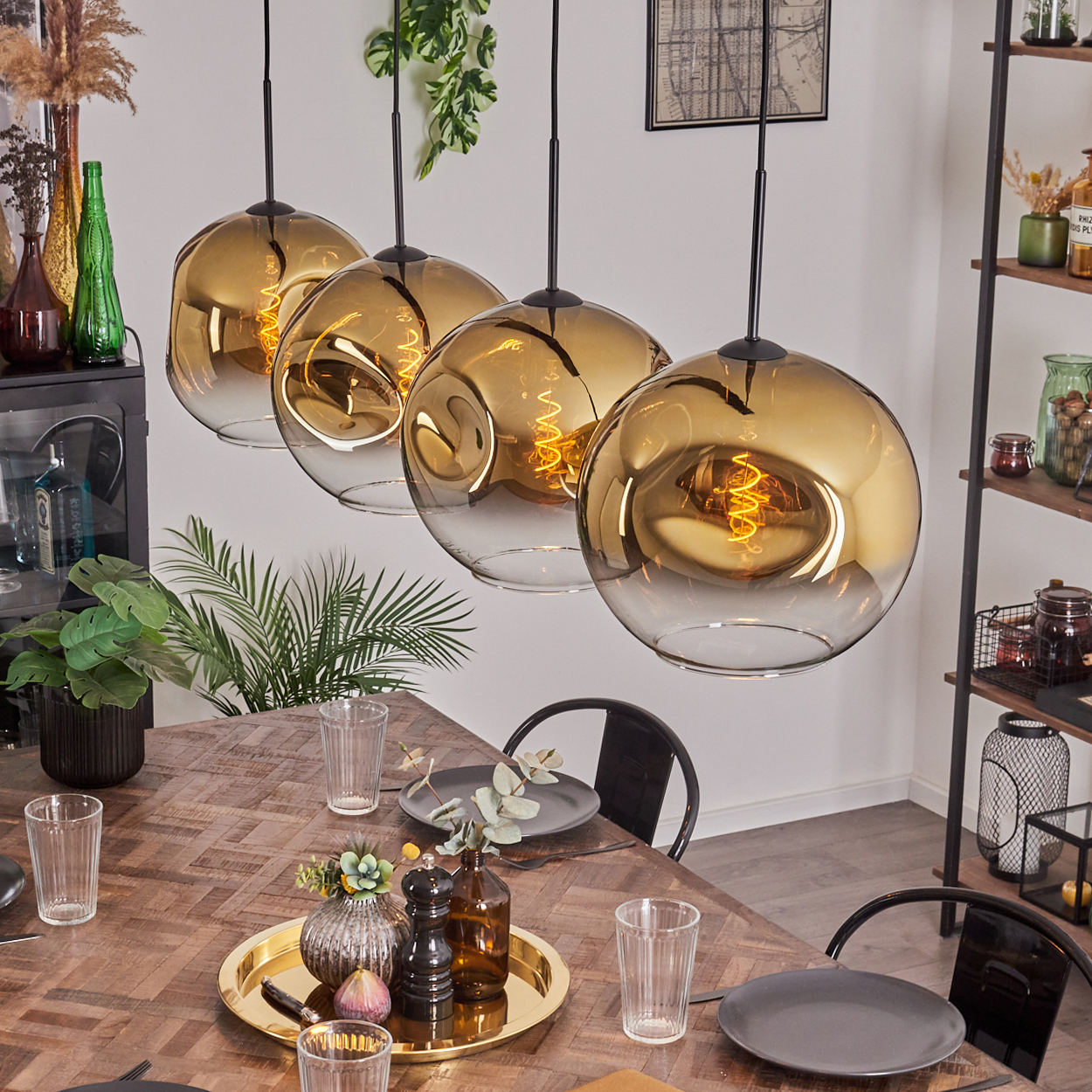 Esszimmer mit Holztisch. Vier goldene Hängelampen hängen darüber. Teller, Gläser und Dekoration befinden sich auf dem Tisch.