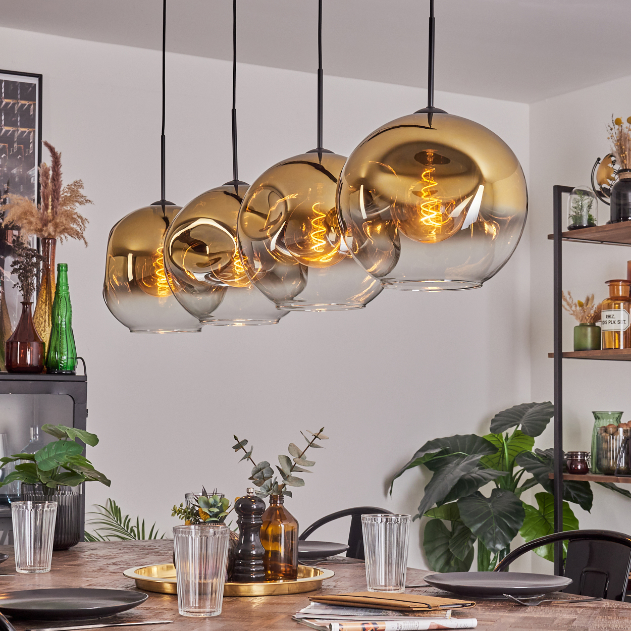 Esszimmer mit gedecktem Holztisch. Darüber hängen fünf goldfarbene Kugelleuchten. Pflanzen und Dekoration sind ebenfalls vorhanden.