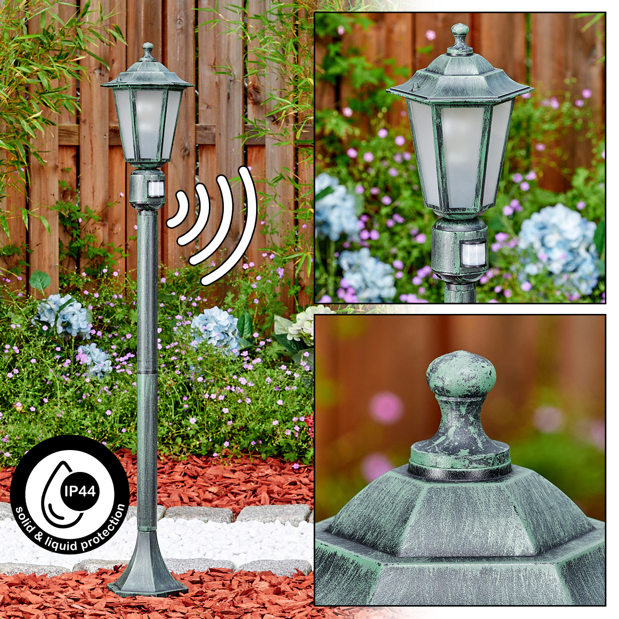 Eine grüne Außenlampe mit IP44-Schutz steht in einem Garten. Der Hintergrund zeigt Blumen, einen Holzzaun und roten Mulch.