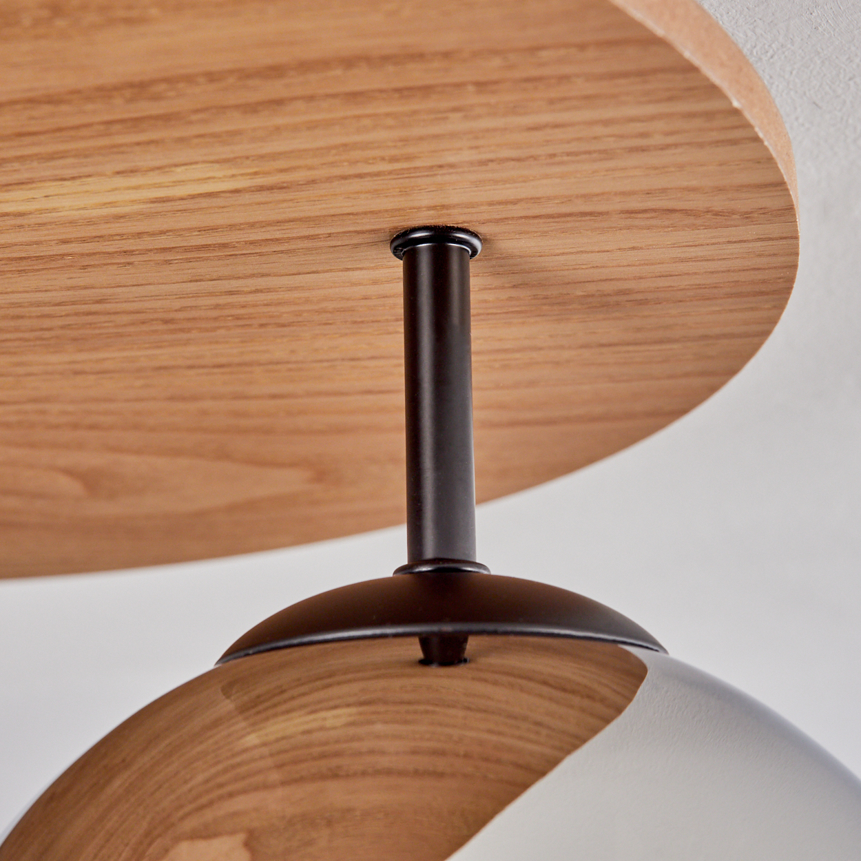 Nahaufnahme einer Holzlampenbefestigung mit dunkler Metallstange und klarem, reflektierendem Glasschirm.