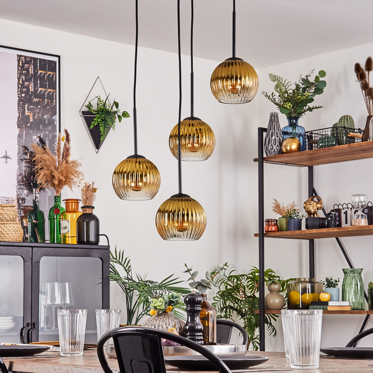 Esszimmer mit goldenen Hängeleuchten. Tisch mit Gläsern gedeckt. Regale mit Deko und Pflanzen.