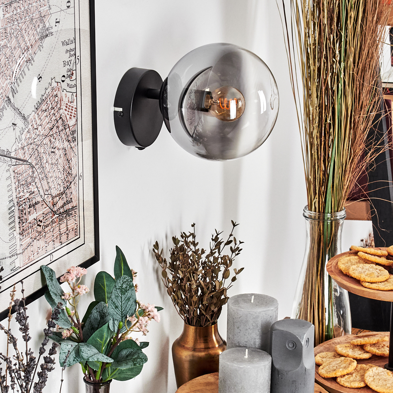 Eine moderne Wandlampe mit Glasschirm, Karte, Pflanzen, Kerzen und Snacks auf einem Tisch. Die Lampe ist schwarz und der Schirm ist rund.