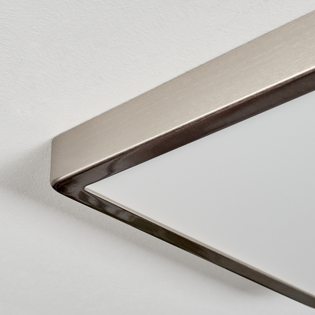 Nahaufnahme einer rechteckigen Leuchte mit Metallrahmen. Die Leuchte befindet sich vor einer weißen, strukturierten Wand.