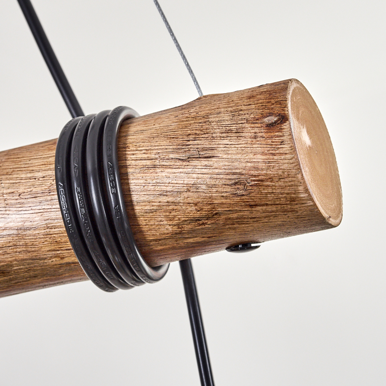 Nahaufnahme eines Holzstamms mit schwarzen Kabeln. Drähte und ein Metallkabel hängen ihn vor weißem Hintergrund auf.